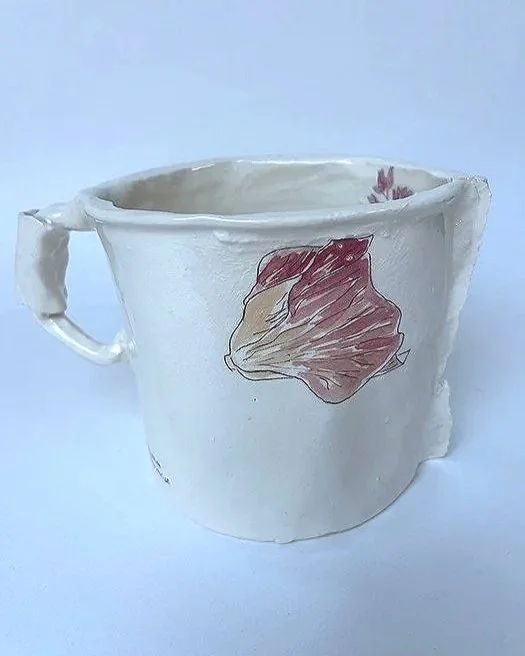 White ceramic mug with a hand-painted flower design, chipped edges, and uneven surface.