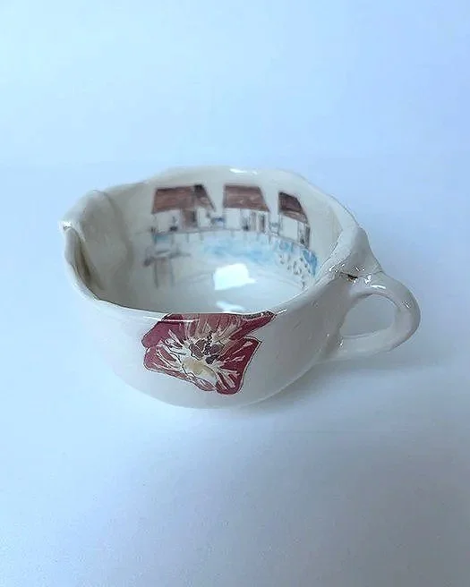 A small, white ceramic teacup with a floral pattern on the outside and a reflection of a room with windows inside.