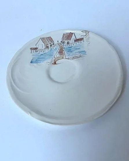 A decorative plate with a painted winter scene of houses and a dock on a frozen lake.