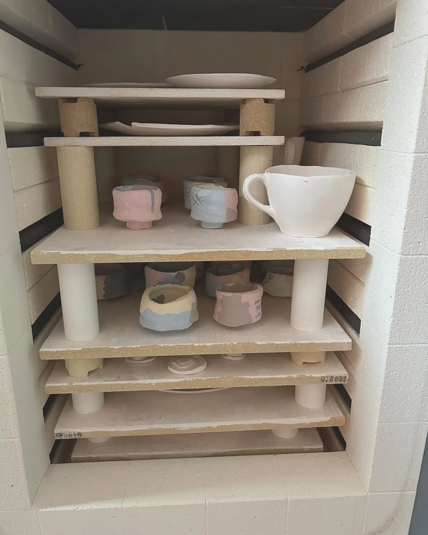 Empty pottery kiln with unglazed ceramic cups, bowls, and plates on shelves.