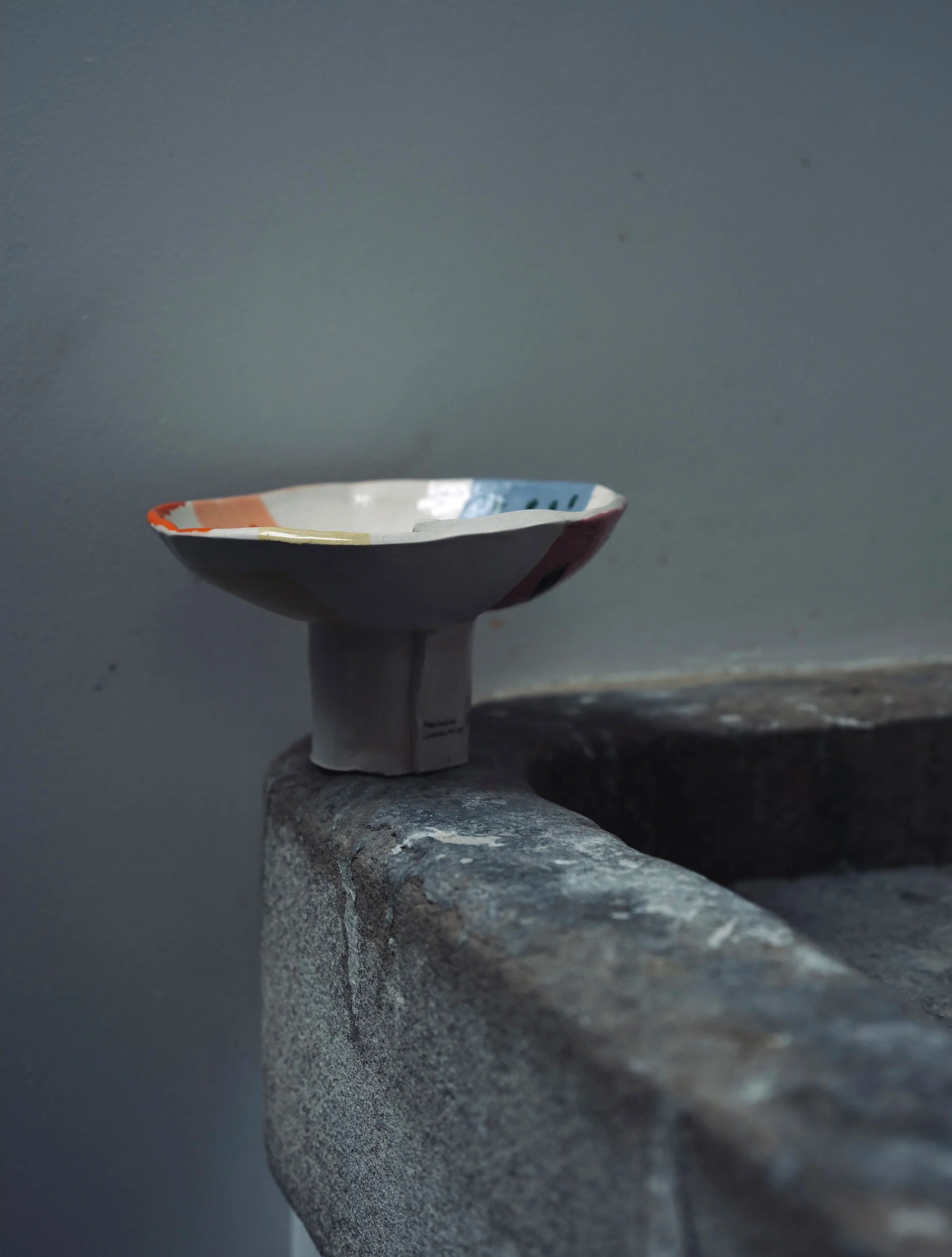 Close-up of a small, colorful ceramic bowl placed upside down on a gray stone surface against a gray background.