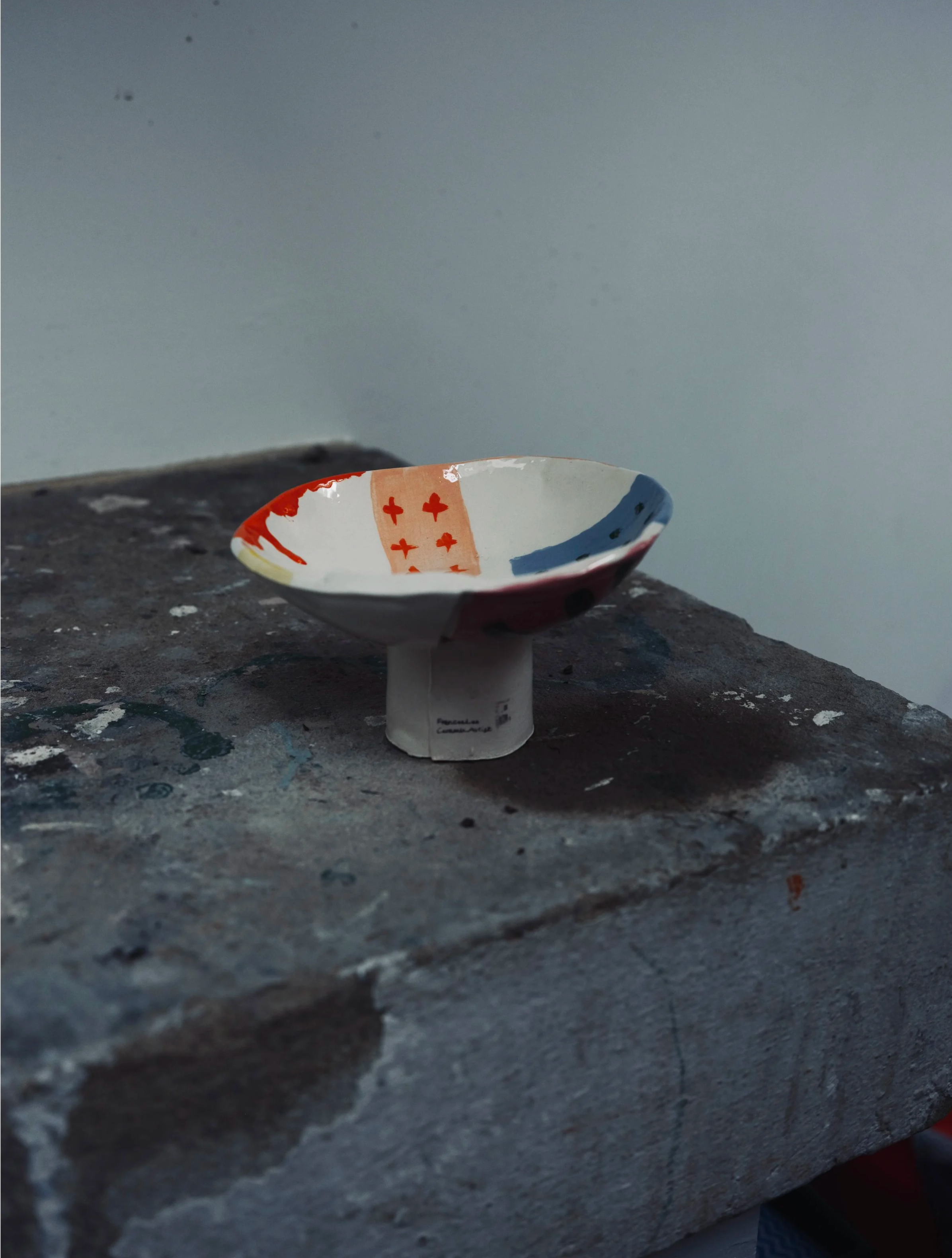 A small, decorated ceramic bowl resting on a rough, gray stone surface.