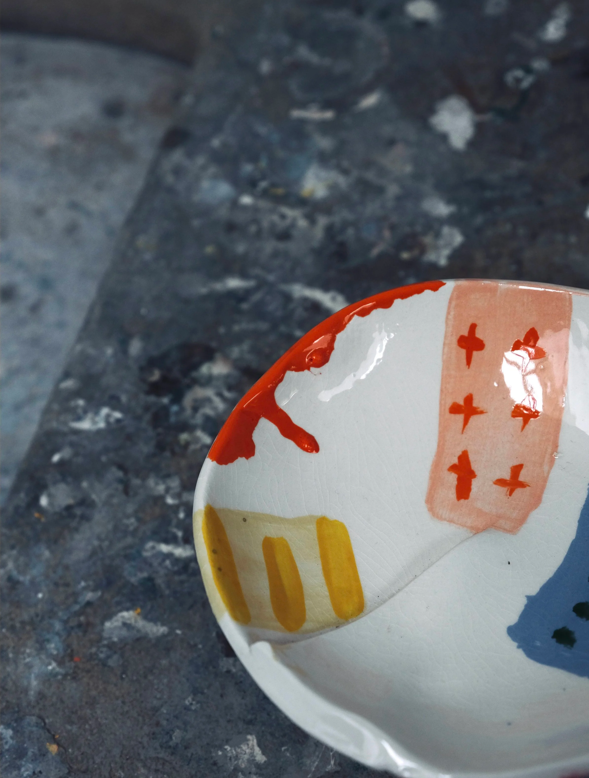 Part of a decorative ceramic plate with yellow, orange, and red patterns, held against a grey, speckled surface.