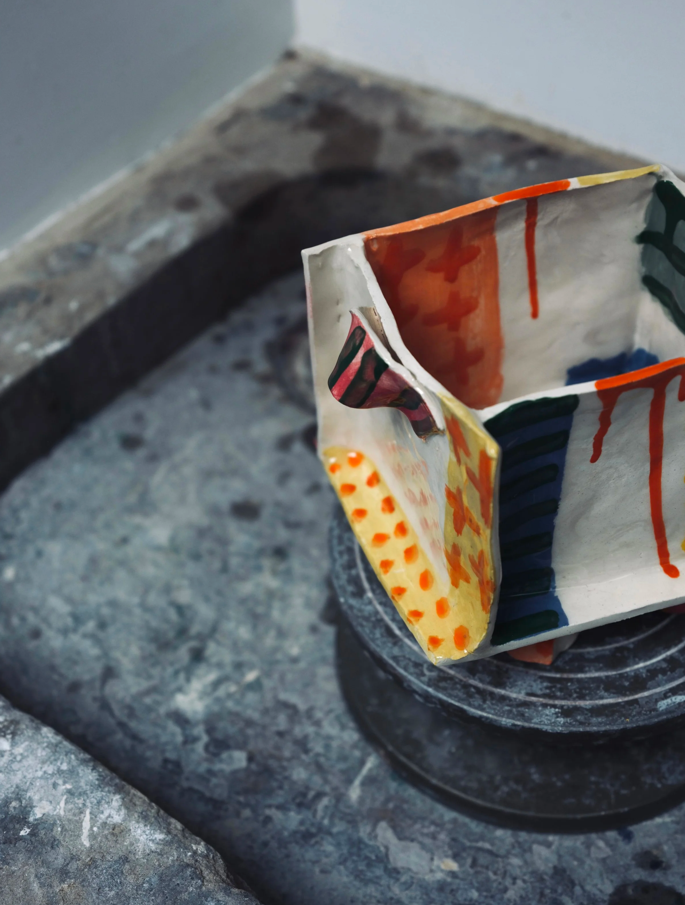 Close-up of a colorful, abstract painted ceramic mug placed on a dark stone surface.