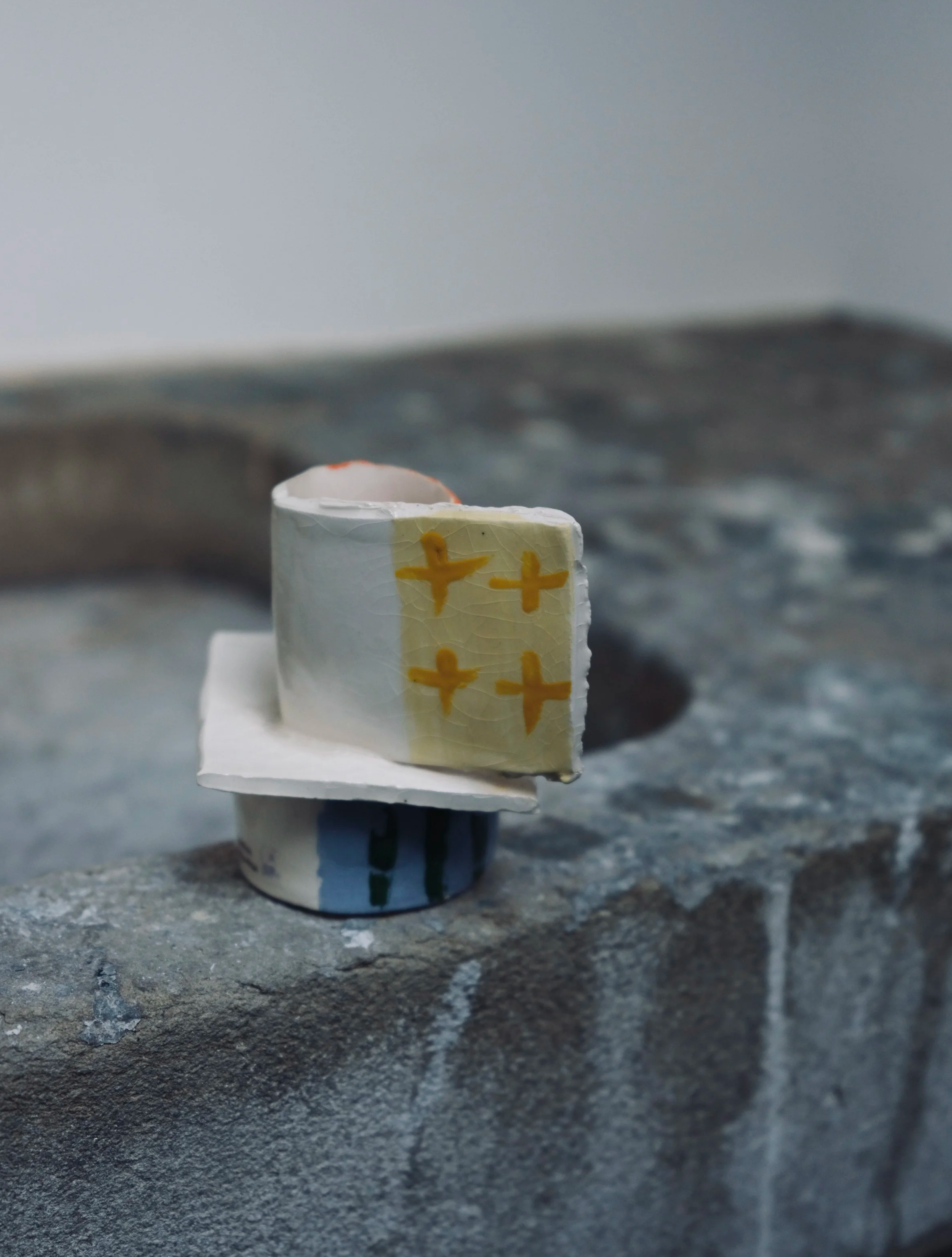 Close-up image of a small three-layered cake with smooth white icing, decorated with yellow crosses, placed on a textured gray surface.