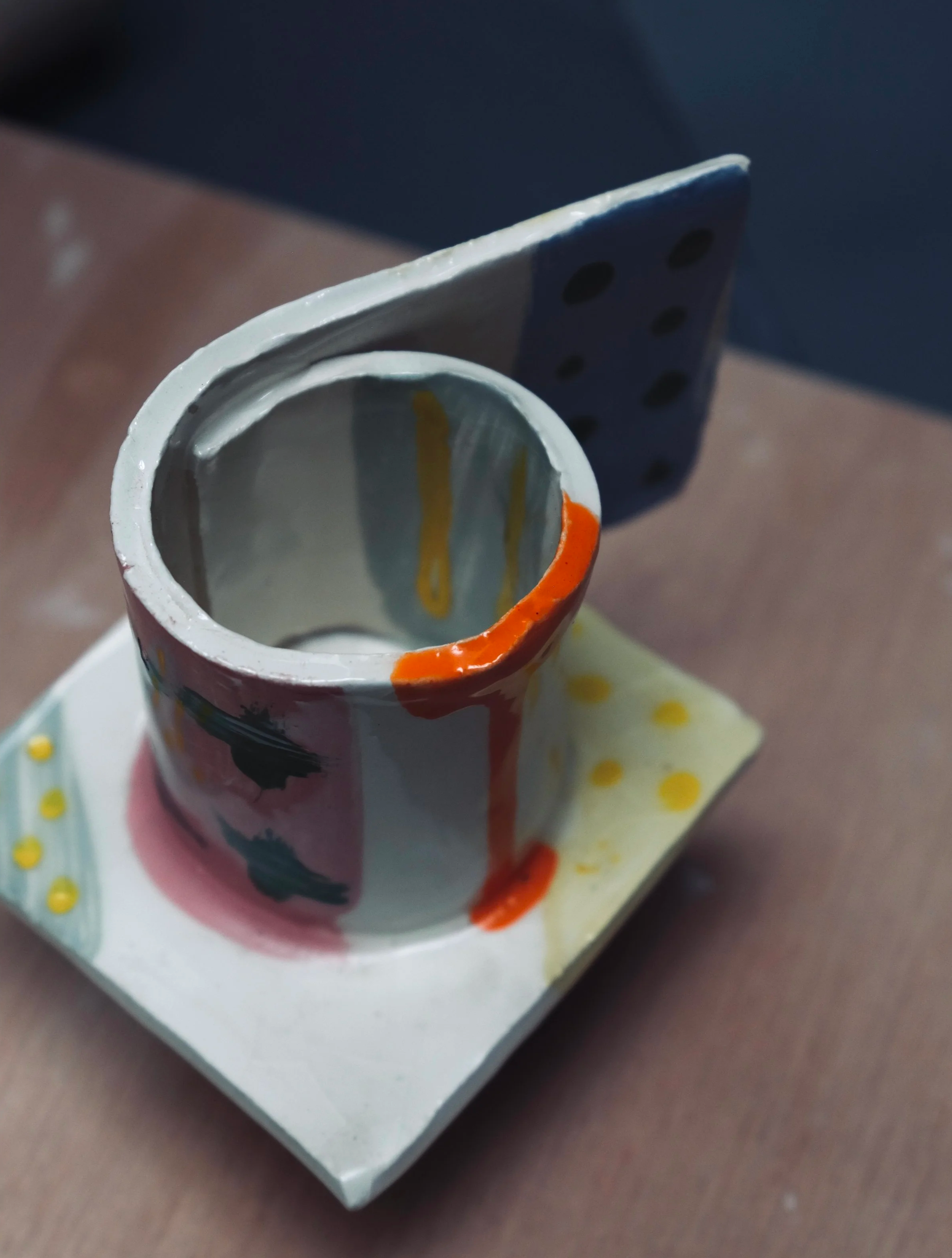 Close-up photo of a small, decorative ceramic cup with colorful painted designs on a polka dot paper napkin.
