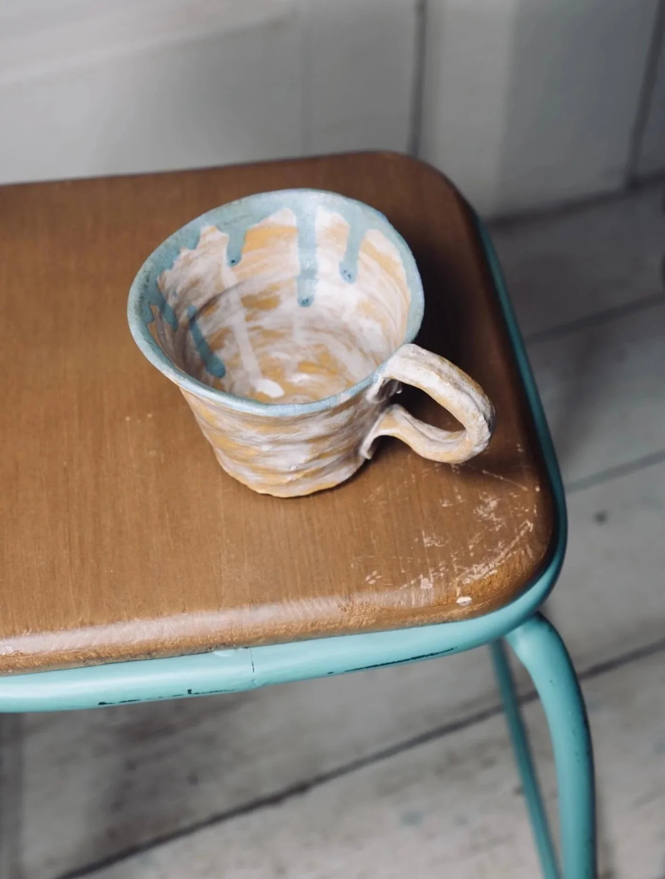 Empty ceramic mug with a swirl pattern in beige, light blue, and white, sitting on a wooden table with a metal frame, next to a gray wall and a gray cabinet.