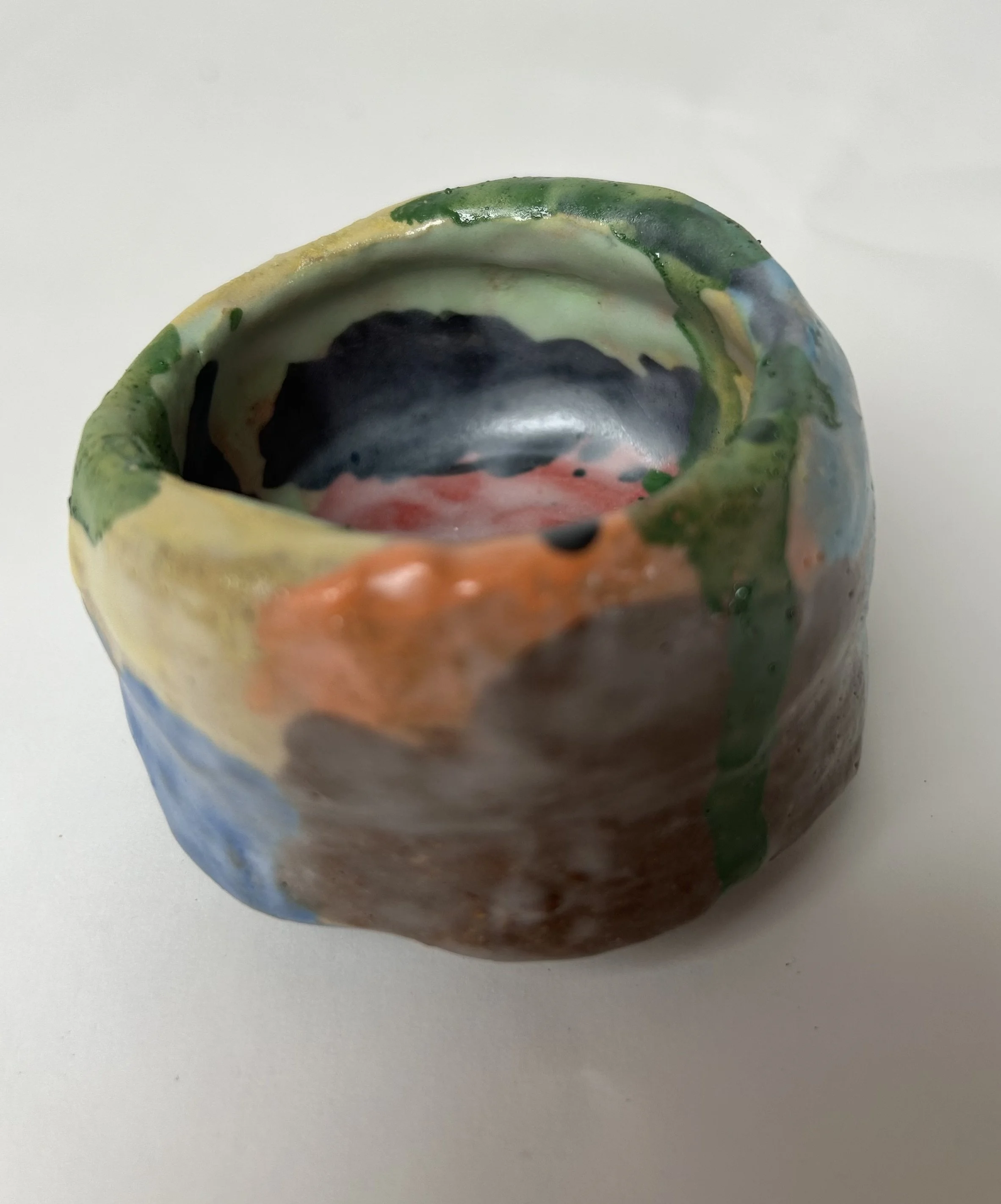 A ceramic mug with a colorful, abstract pattern featuring green, black, pink, and blue hues, placed on a white surface.