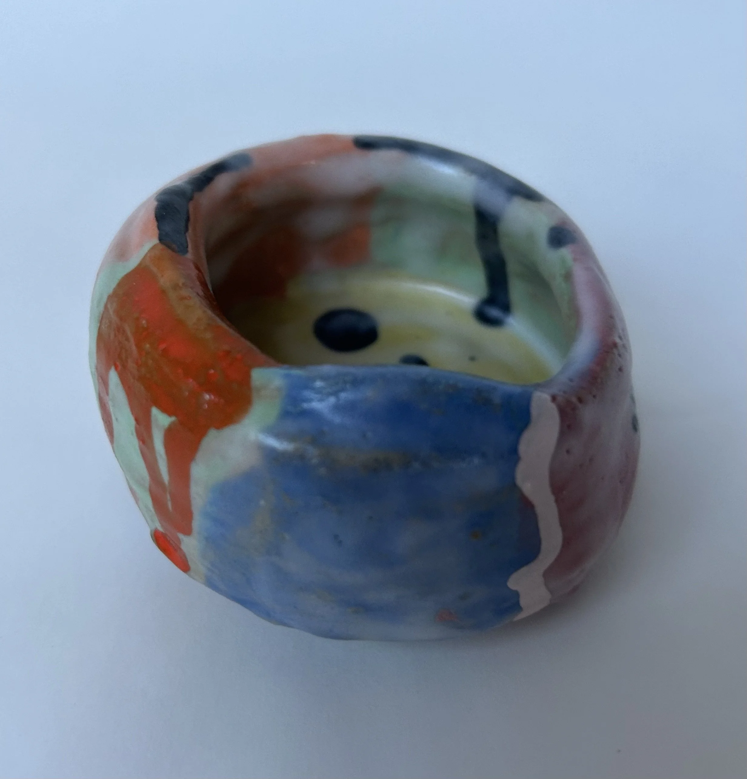Close-up of a colorful painted ceramic or glass object, possibly a decorative item, with a mix of red, blue, yellow, and black colors, against a plain light background.