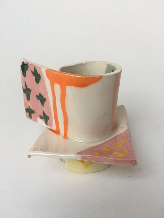 A ceramic mug with an irregular shape and colorful painted designs, including pink, green, orange, and yellow accents.