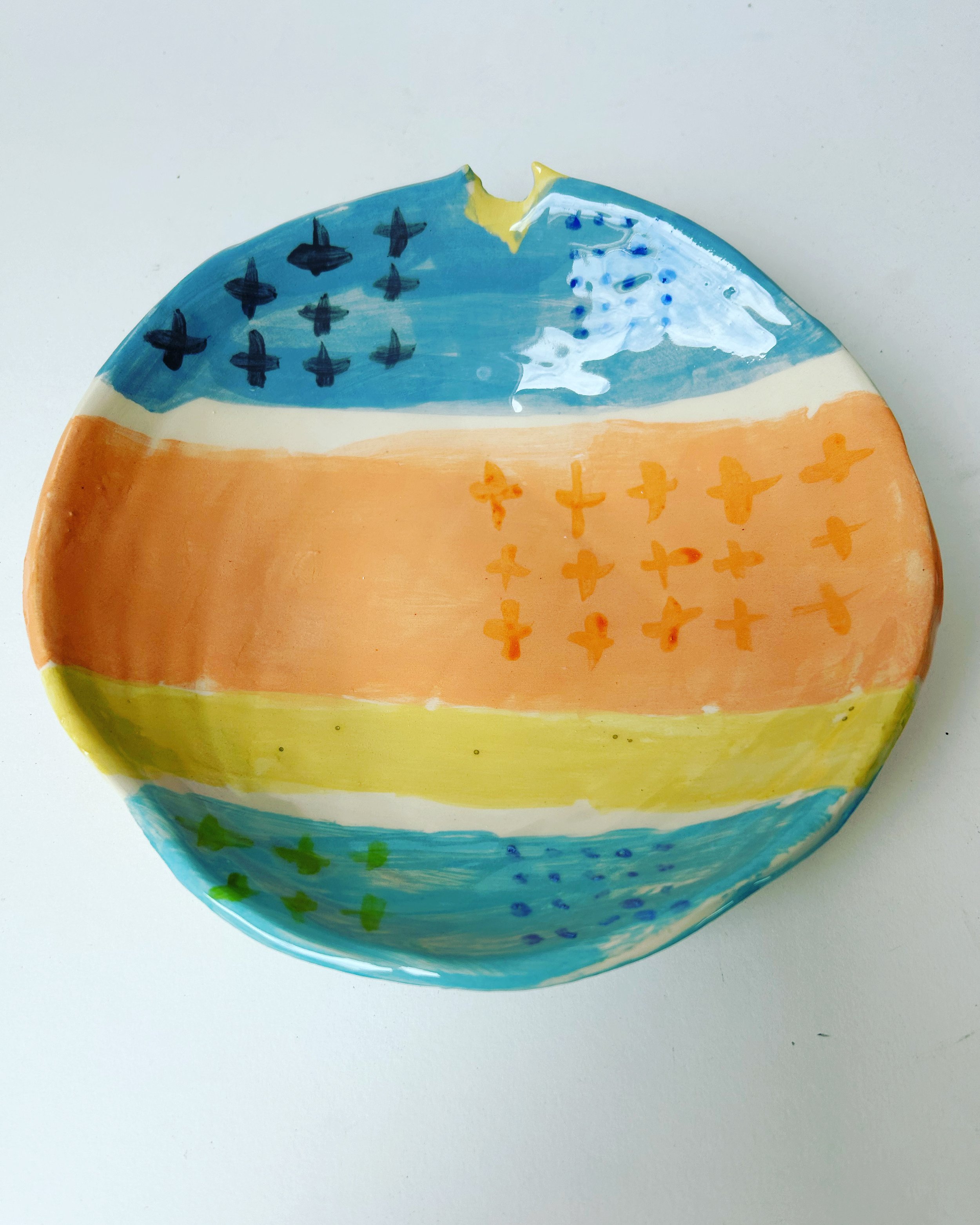 Colorful hand-painted ceramic bowl with abstract designs in blue, yellow, and orange on a white background.
