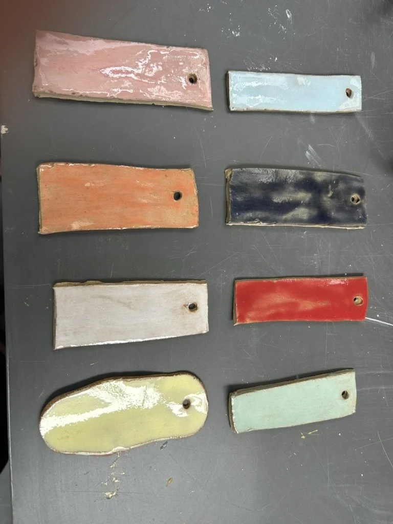 Eight colorful ceramic tiles with holes, placed on a dark gray surface.