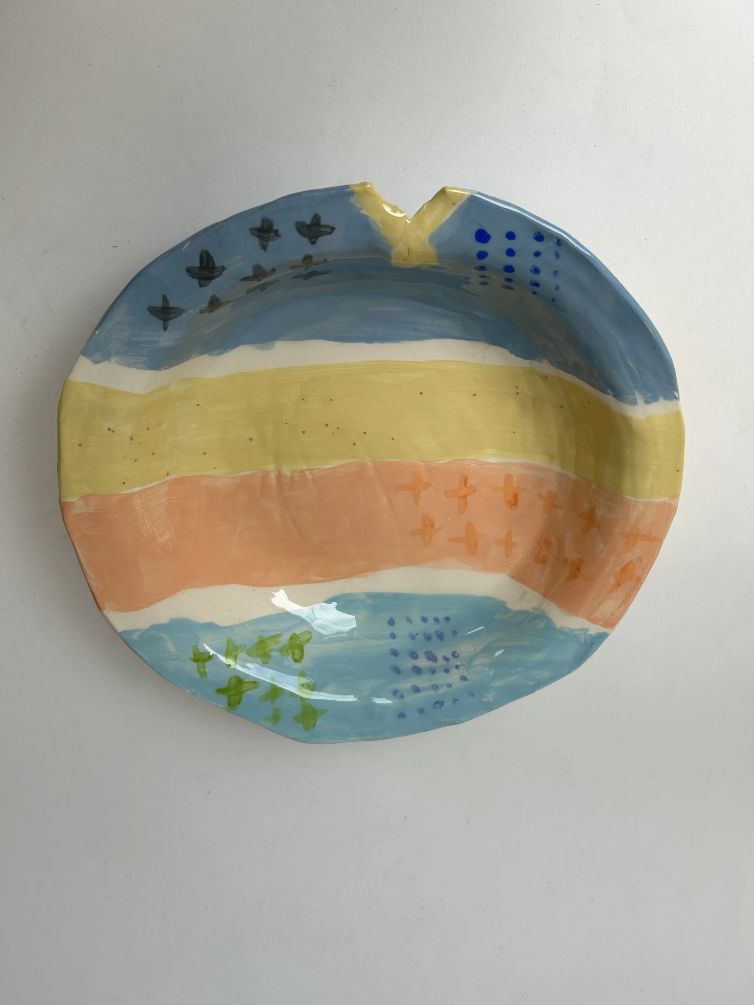 A colorful, hand-painted ceramic plate featuring abstract patterns and stripes in blue, yellow, orange, and green with decorative elements.