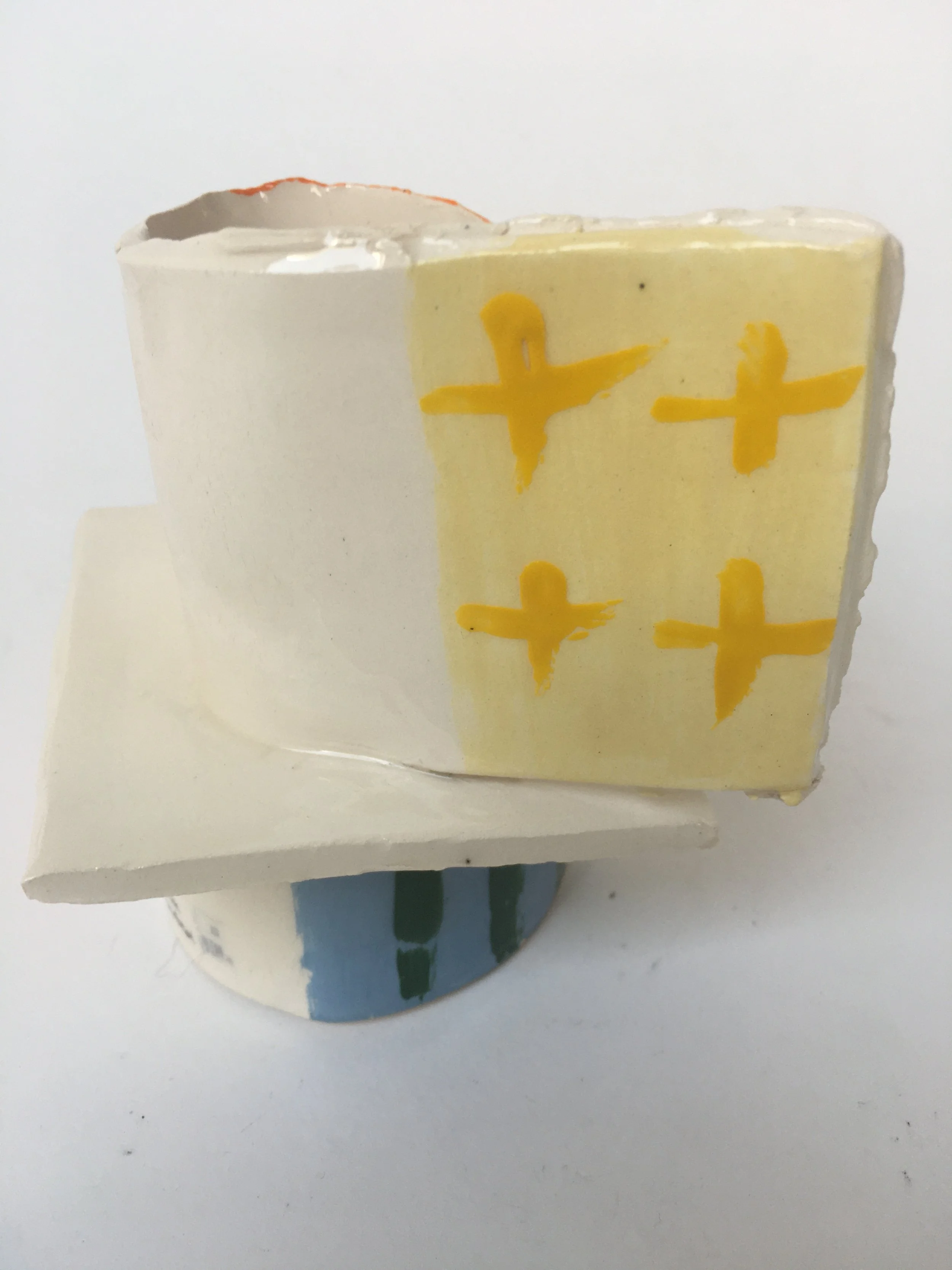 Close-up of a broken ceramic or plastic object with yellow and black cross-like designs on the yellow portion, placed on a white surface.
