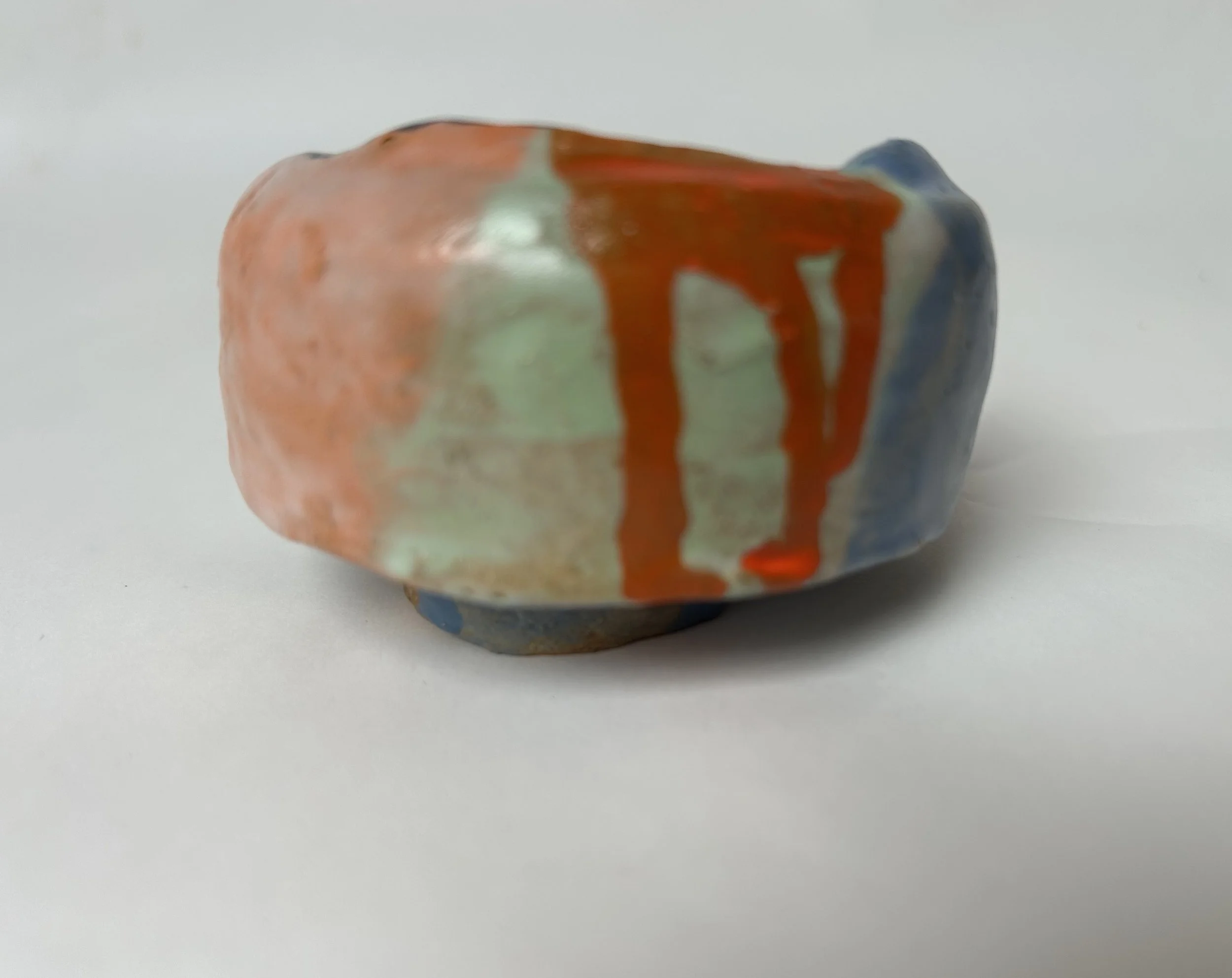 Close-up of a stone with multicolored glaze, primarily orange, blue, and white, on a plain white surface.