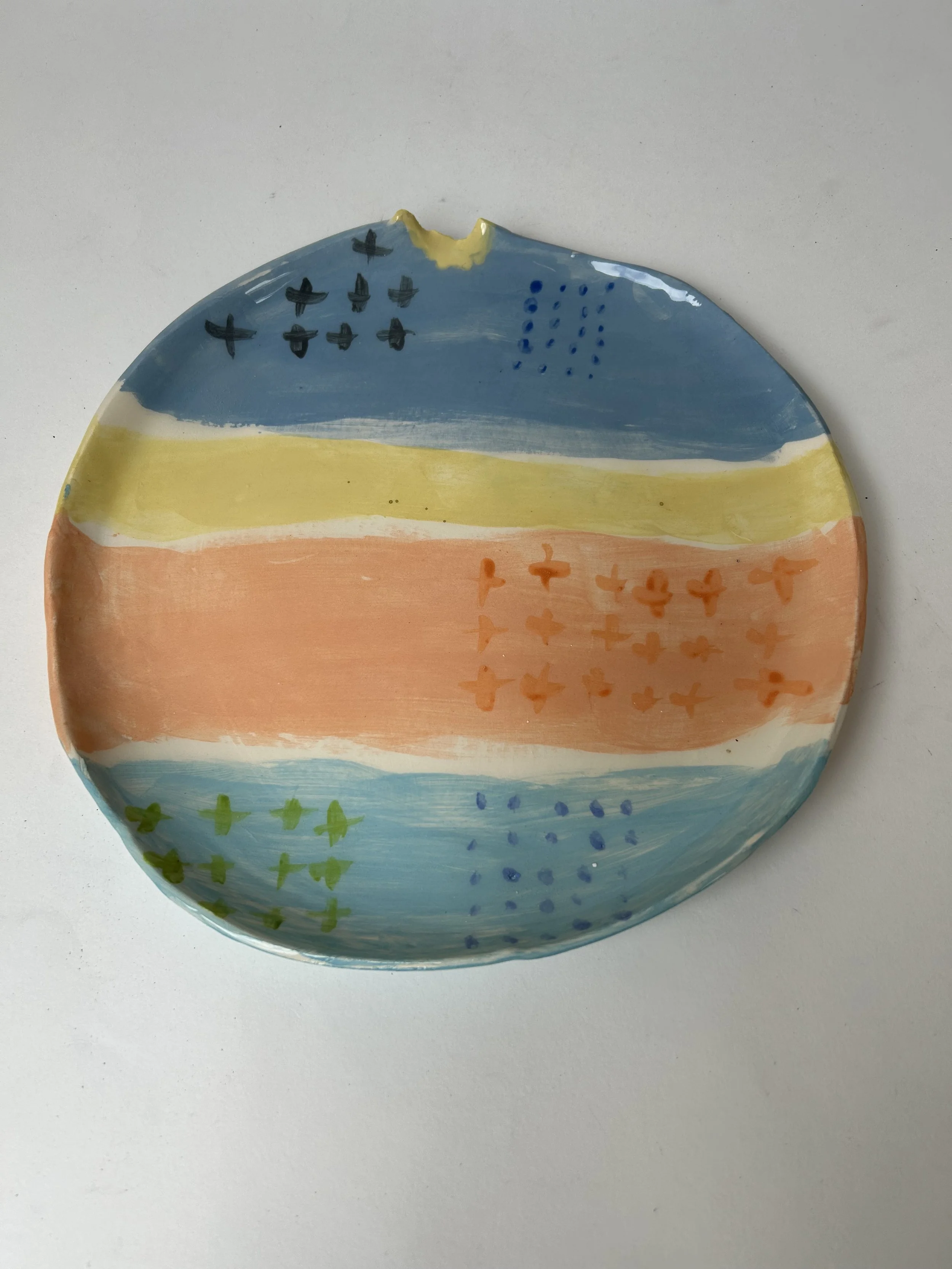 A small, round ceramic plate painted with colorful horizontal stripes and various small patterns.