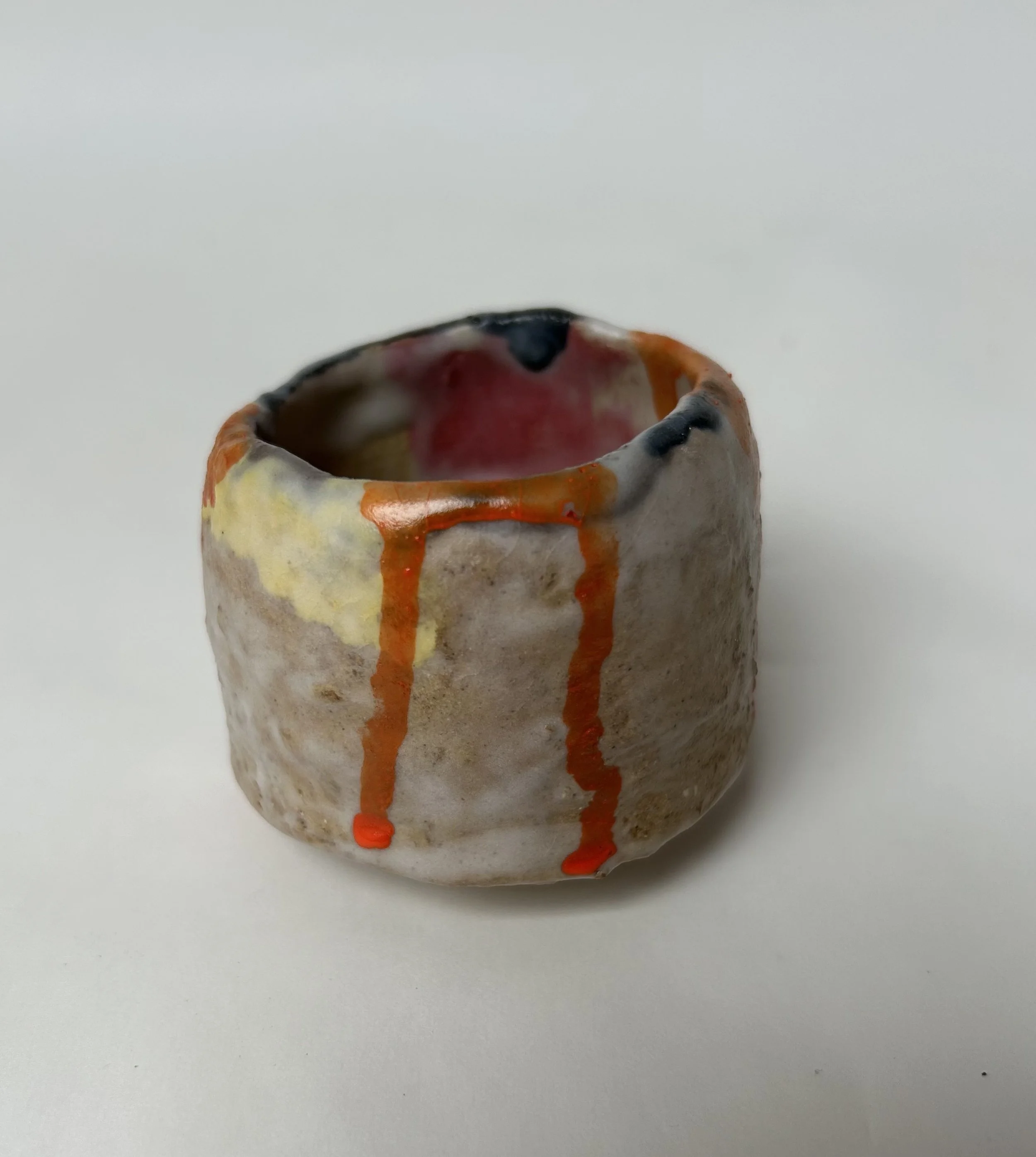 A ceramic mug with a textured beige surface and colorful glaze drips, placed on a white background.