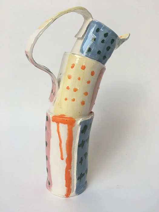 A mixed-media sculpture resembling a stacked set of three colorful, hand-painted ceramic cups with different patterns and a spout, against a plain background.