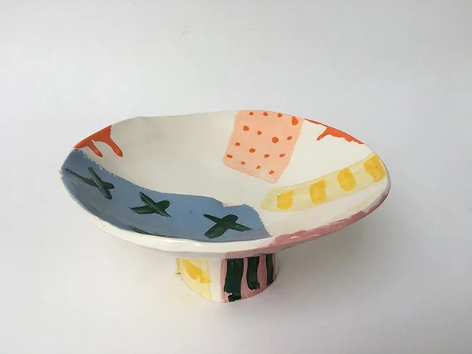 Colorful, hand-painted ceramic bowl with abstract patterns in orange, yellow, pink, green, and blue on a white background.