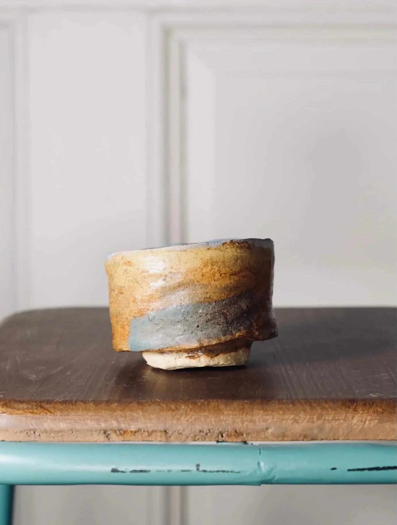 Close-up of a rustic ceramic cup with a glazed, textured surface on a dark wooden surface with a white background.