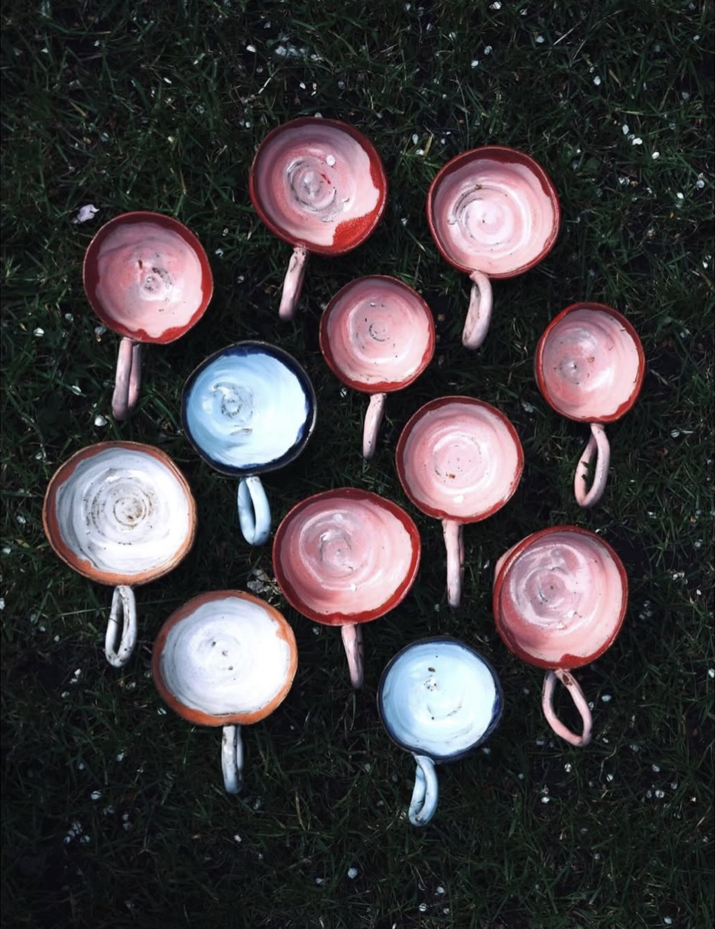 Multiple ceramic coffee cups with handles lying upside down on green grass.