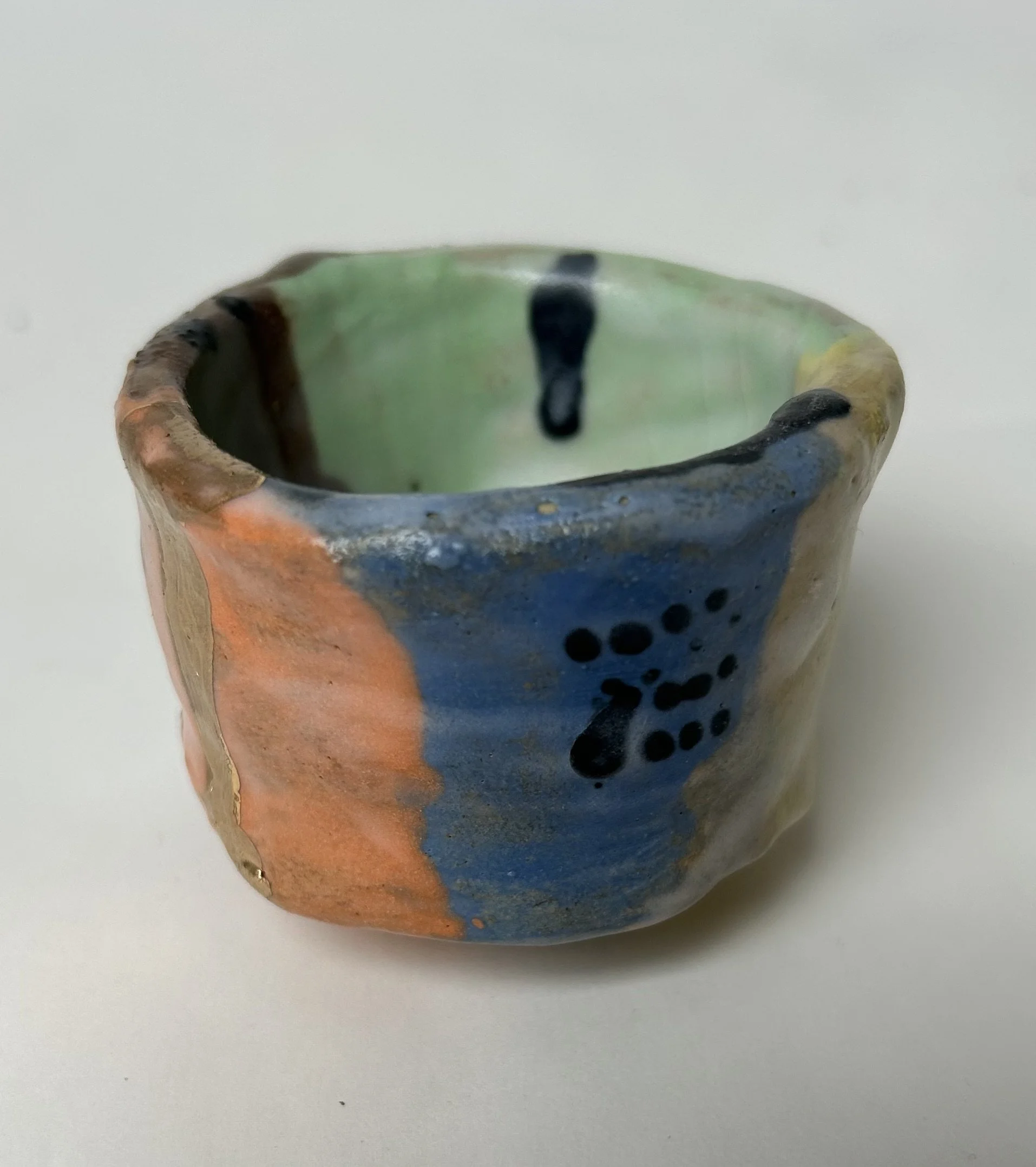 Close-up of a multicolored, handcrafted ceramic cup with abstract design and glaze, set against a plain white background.