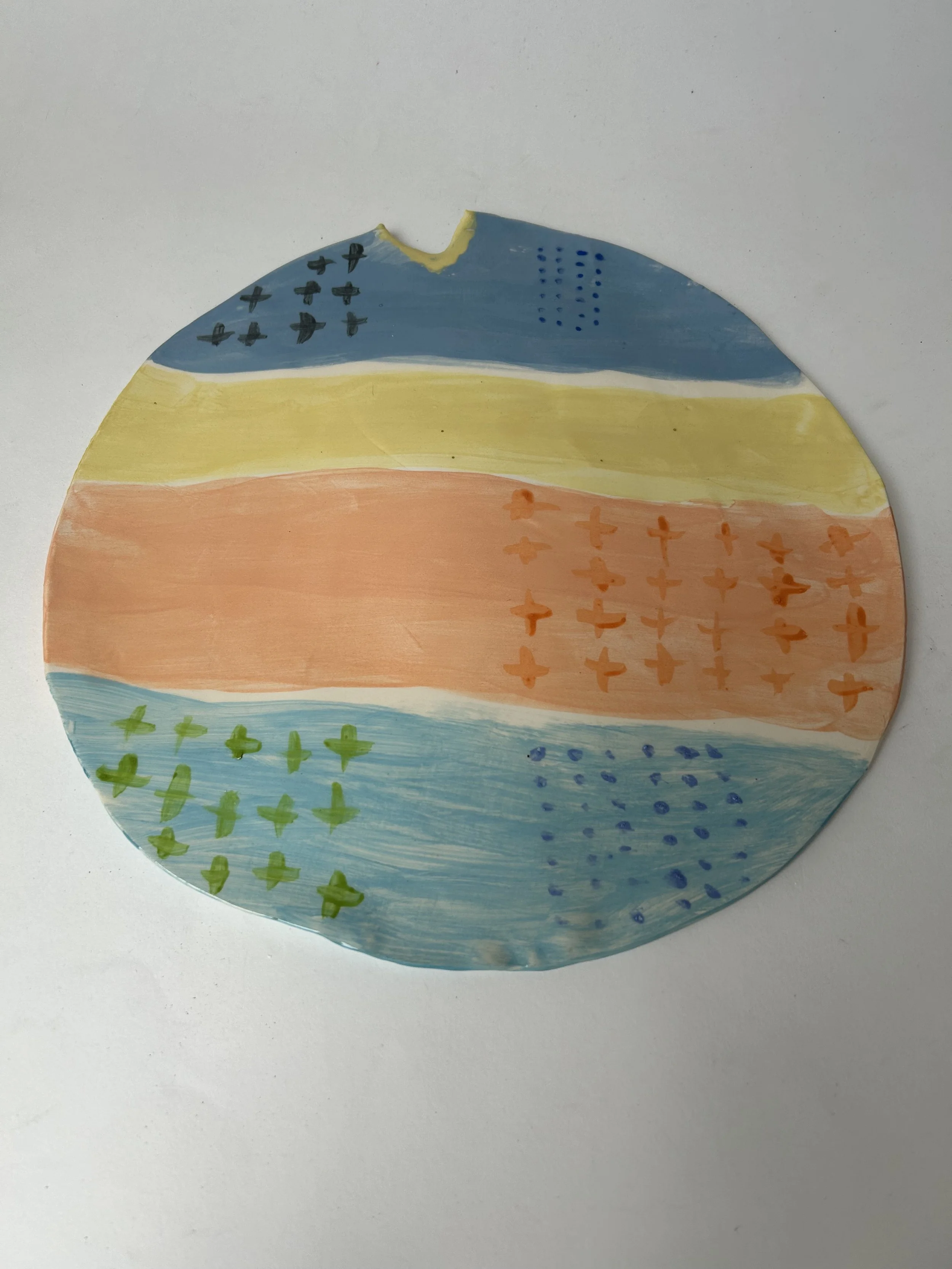 Round paper plate decorated with colorful horizontal stripes and various small painted symbols.