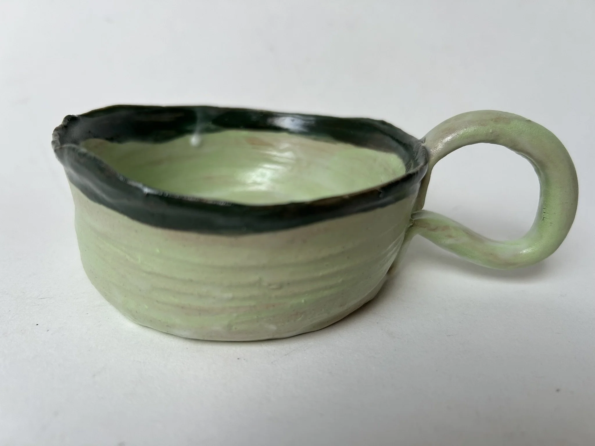 A ceramic pitcher with a pale green body and a dark rim, featuring a curved handle, placed against a plain white background.