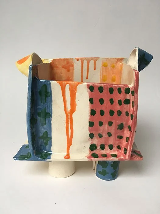 Colorful, hand-painted ceramic sculpture resembling a whimsical building with multiple sections and patterns, mounted on a small pedestal.