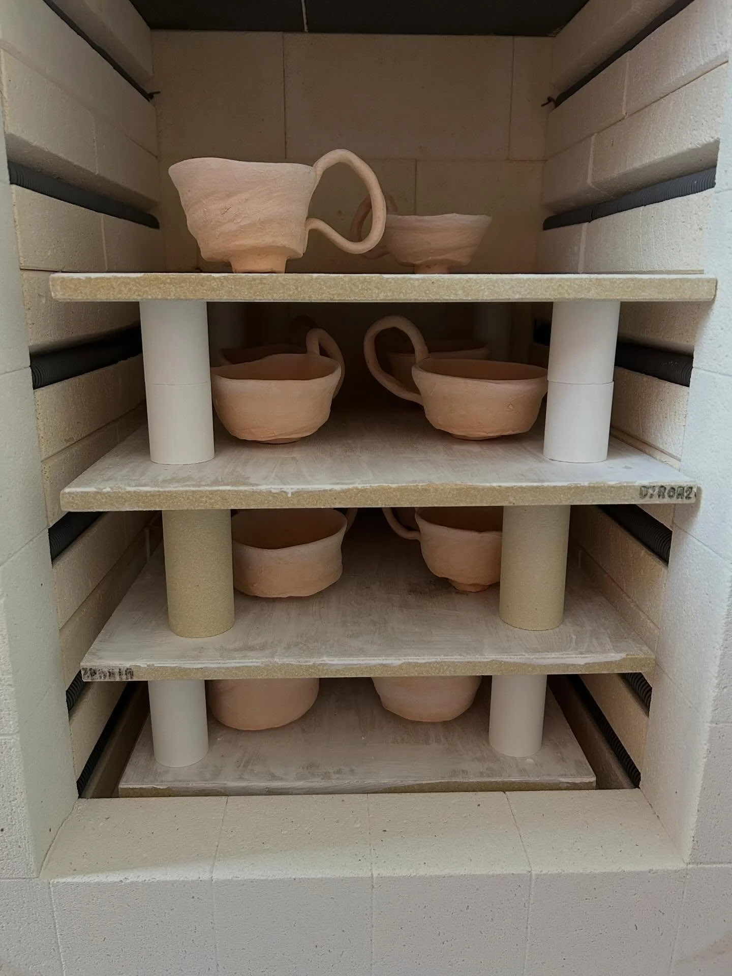 Kitchen cabinet with multiple unglazed ceramic cups on glass shelves inside, with visible support columns.