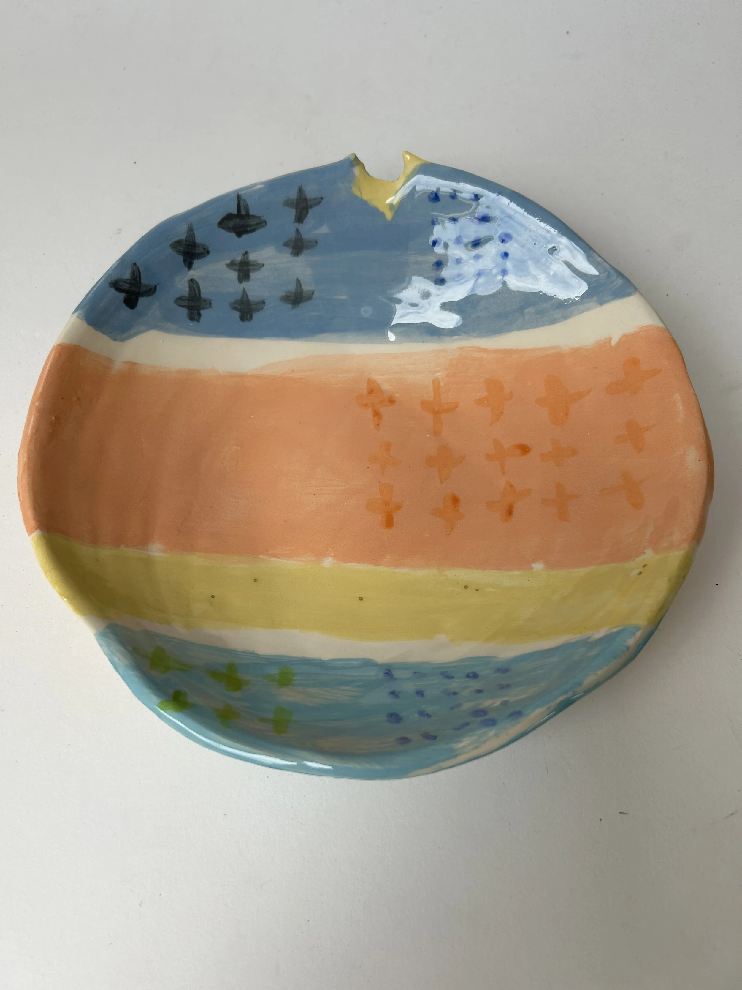 Colorful ceramic plate decorated with painted patterns and designs in blue, yellow, orange, green, and black.