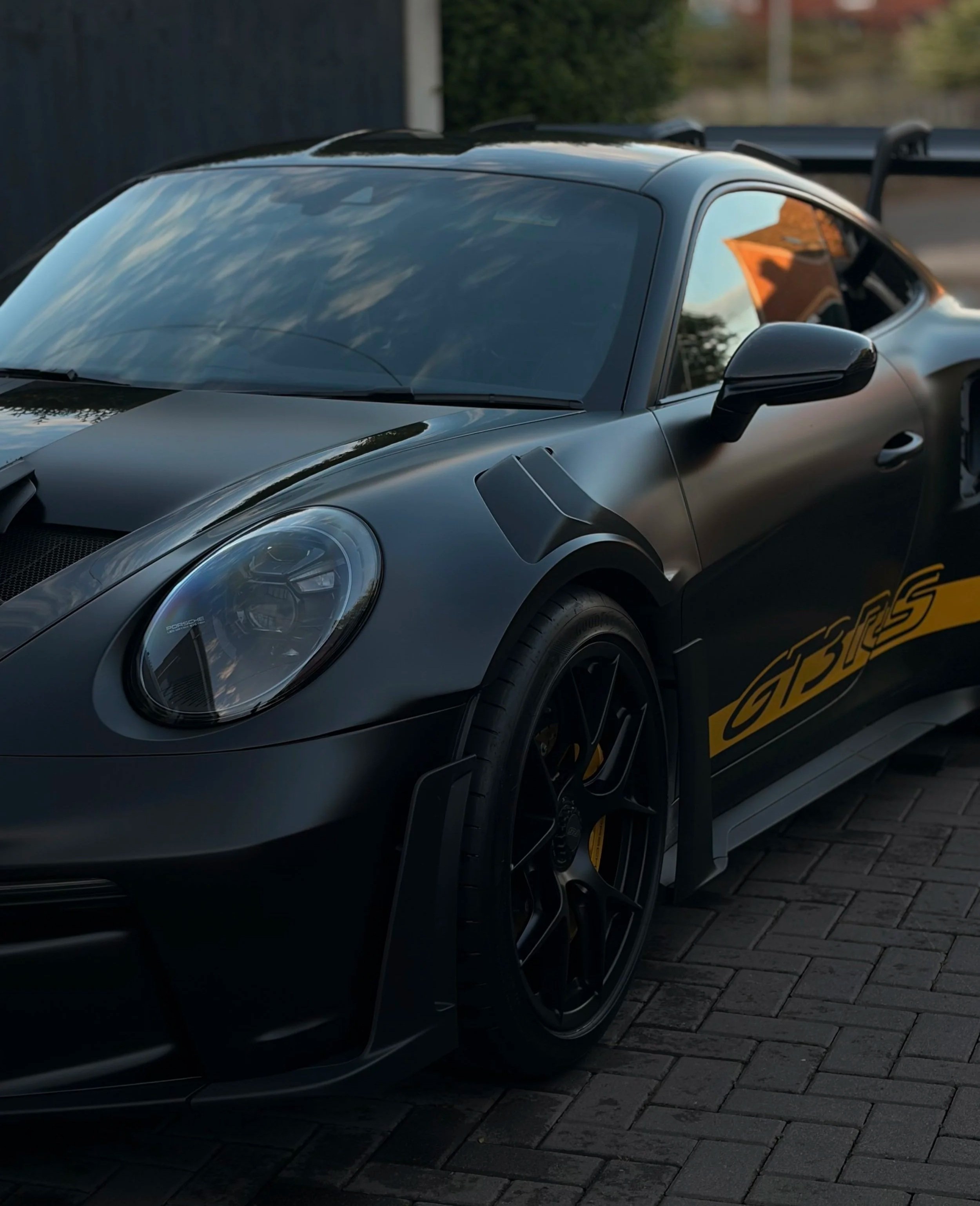 Close-up of a sleek, black Porsche sports car with yellow decals on the side, parked on paving stones.