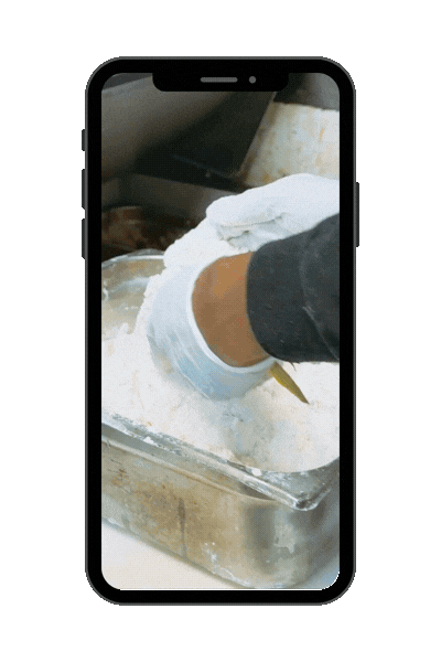 Person wearing gloves mixing or handling a white powdery substance in a metal container.