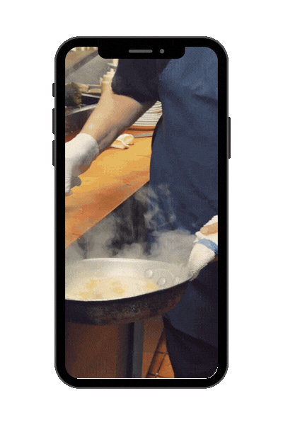 A person cooking on a stove with steam rising, seen through a smartphone screen.