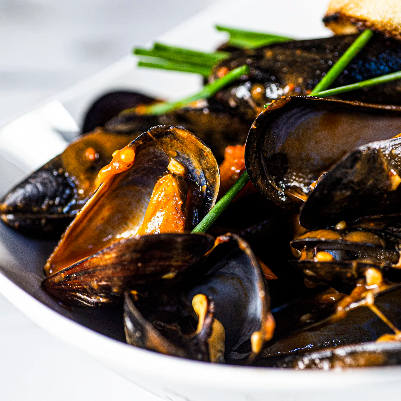 Close-up of cooked mussels with orange sauce, garnished with green chives.