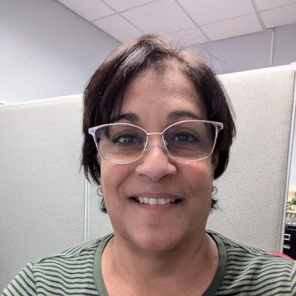 Close-up of a woman with short dark hair, wearing glasses and a green striped shirt, smiling in an office setting. Concord NC promises12 DWI
