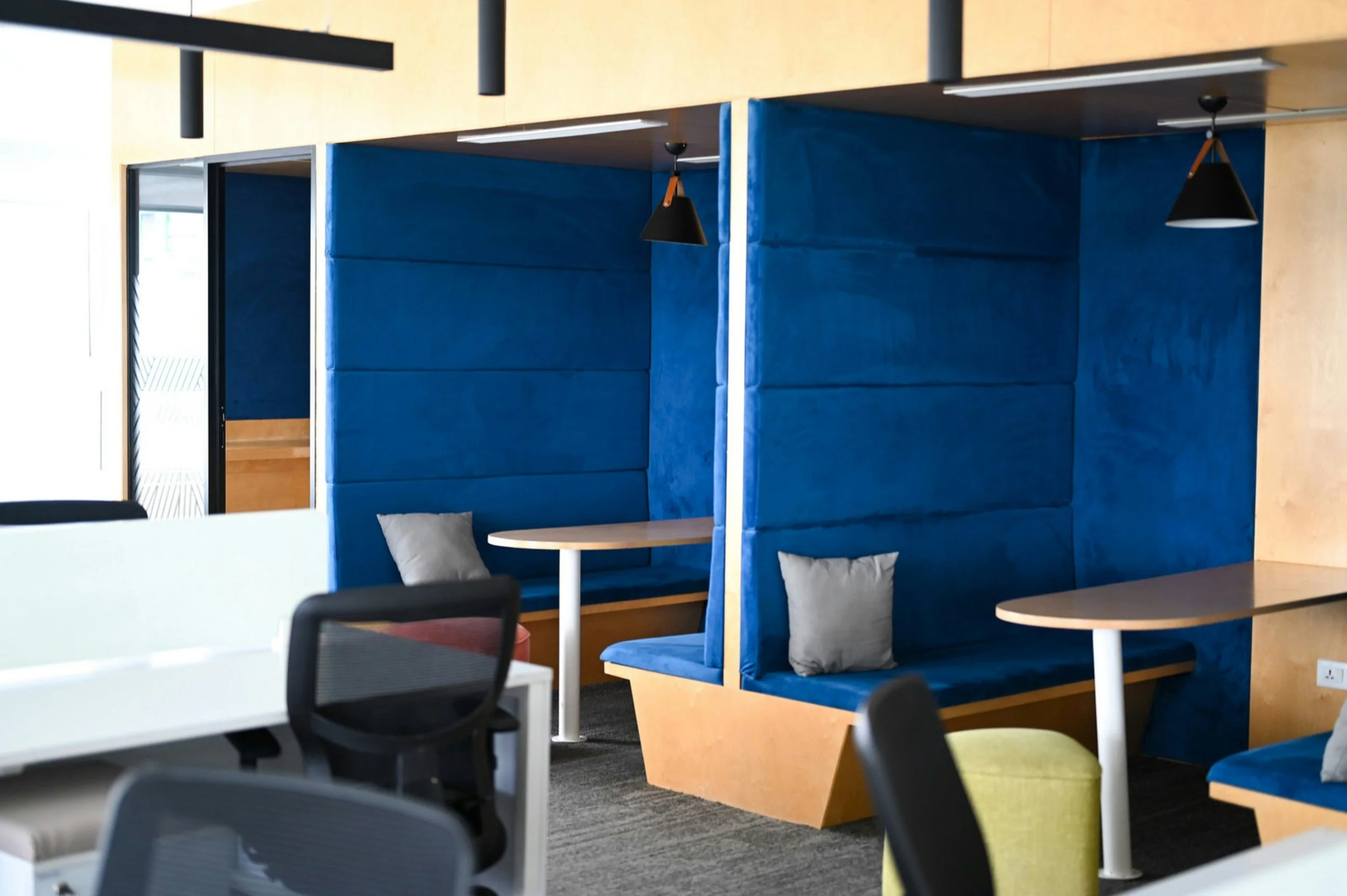 Interior of a modern office or meeting space with blue padded booths, small round tables, and chairs, featuring pendant lighting and a light wood wall. Concord NC promises12 DWI