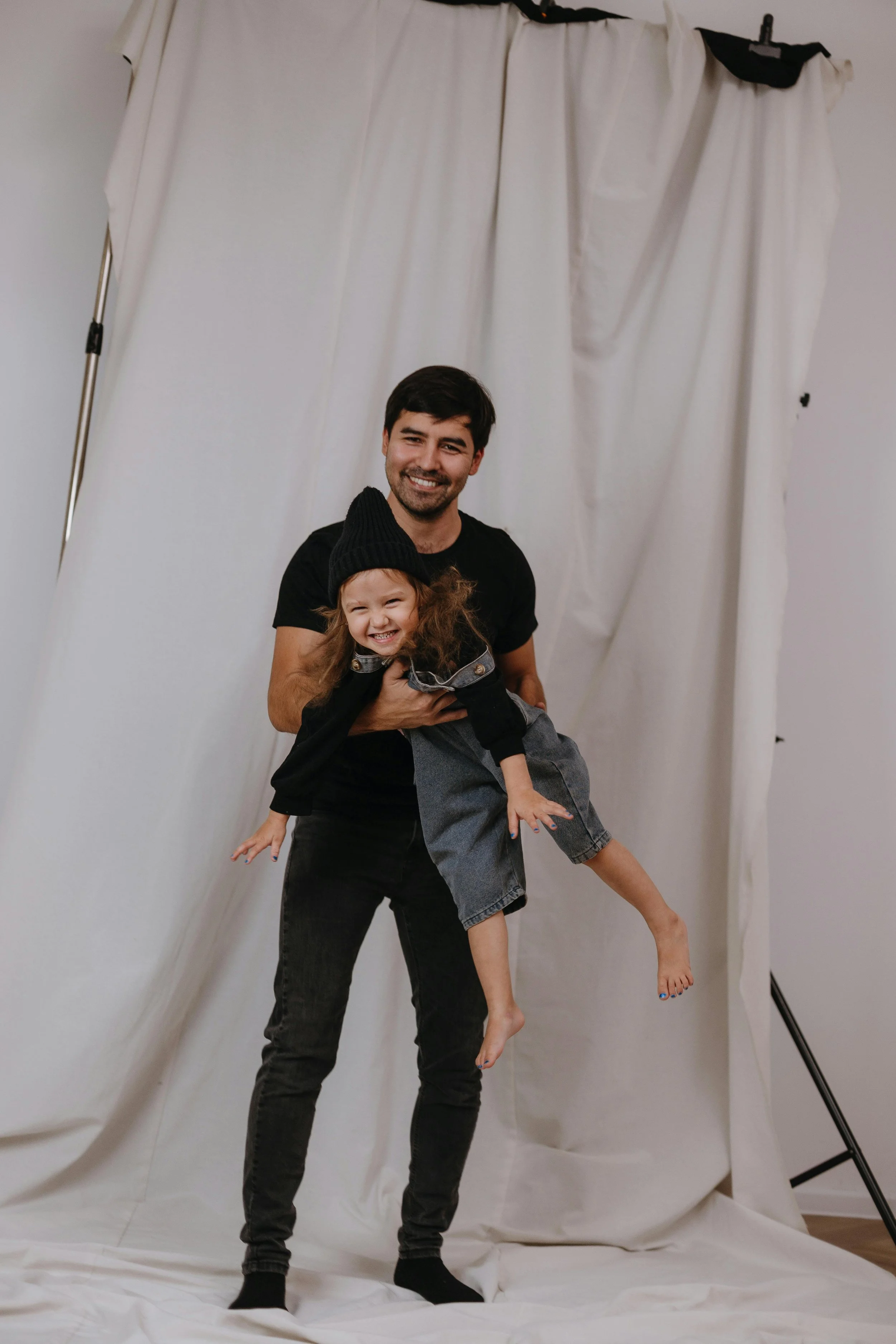A man holding a young girl in a playful pose in front of a white backdrop.