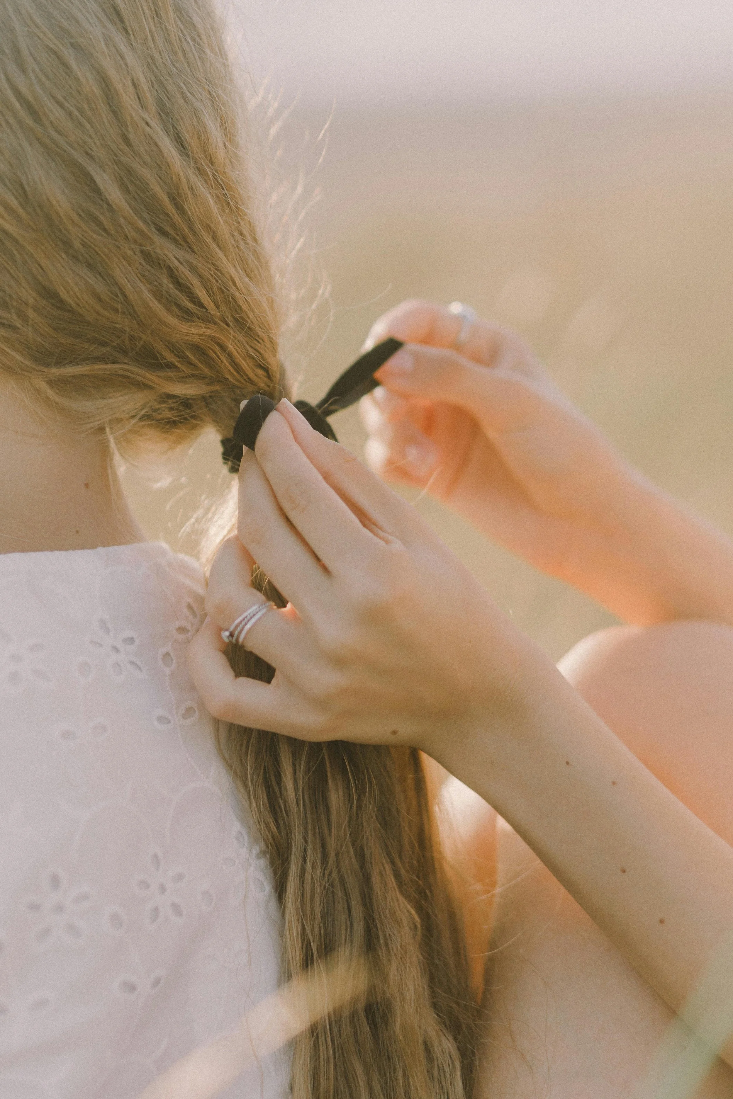 A person with long hair tying it back with a black hair tie