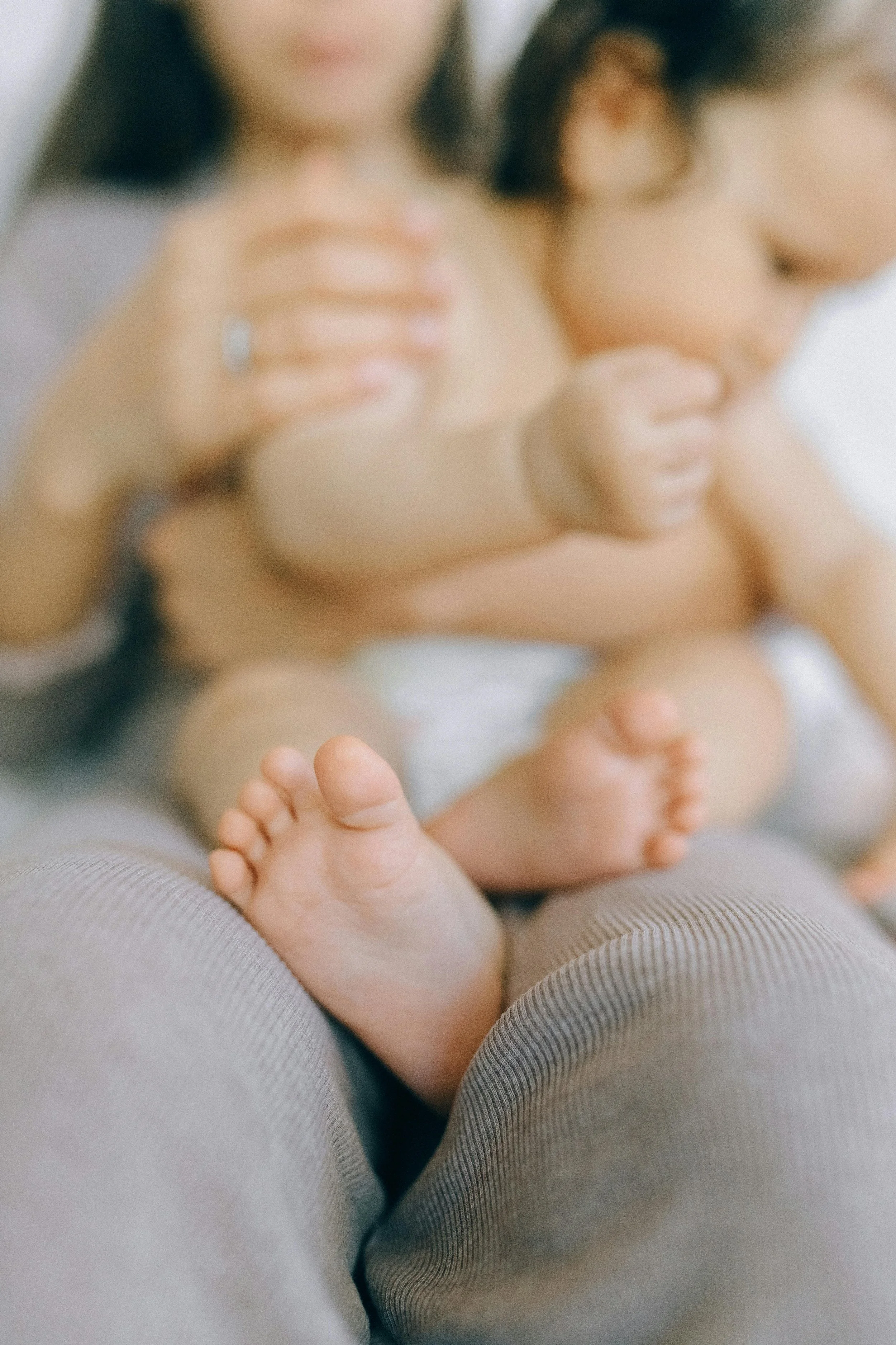 A blurred close-up of a baby laying on someone’s lap, with an adult touching the baby's chest and infant’s hand outstretched towards the camera.