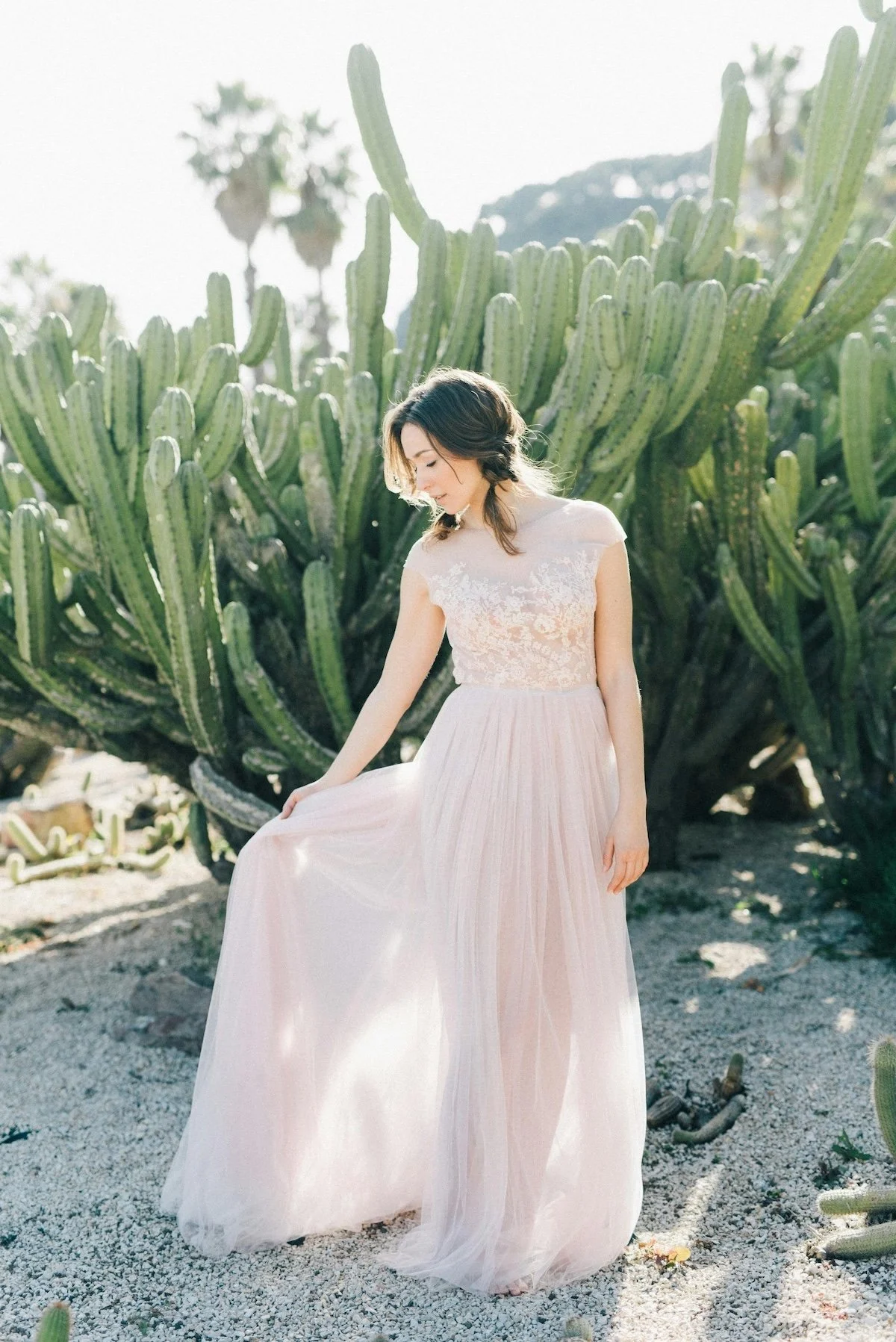 A woman in a light pink, lace top and flowing skirt standing in front of a large cactus plant