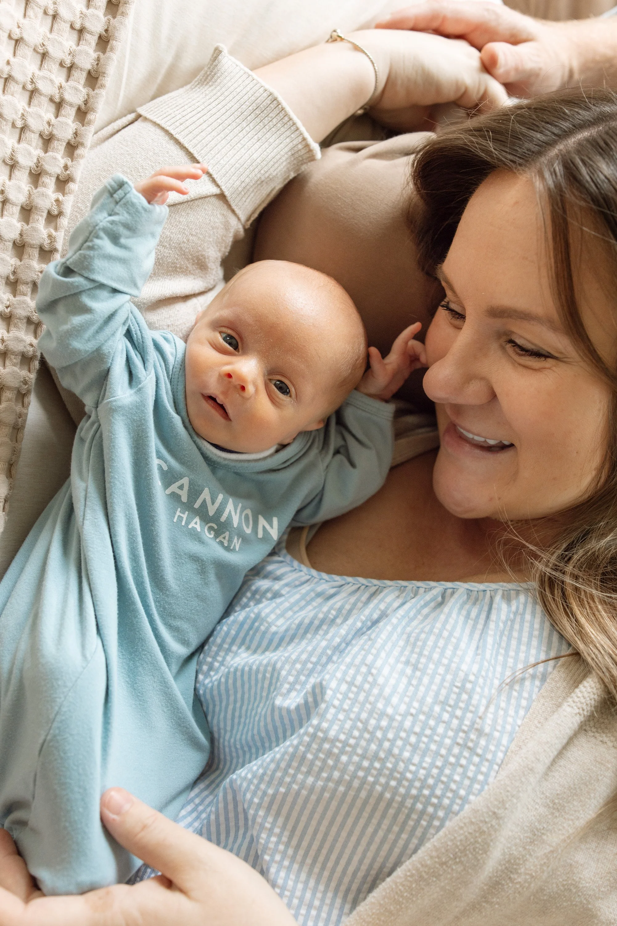 A woman lying on a bed with a young child, both smiling and looking at each other. The woman has long hair, and the child has blonde hair and blue eyes. The woman gently holds the child's hand. The scene has a cozy and loving atmosphere. in home newb