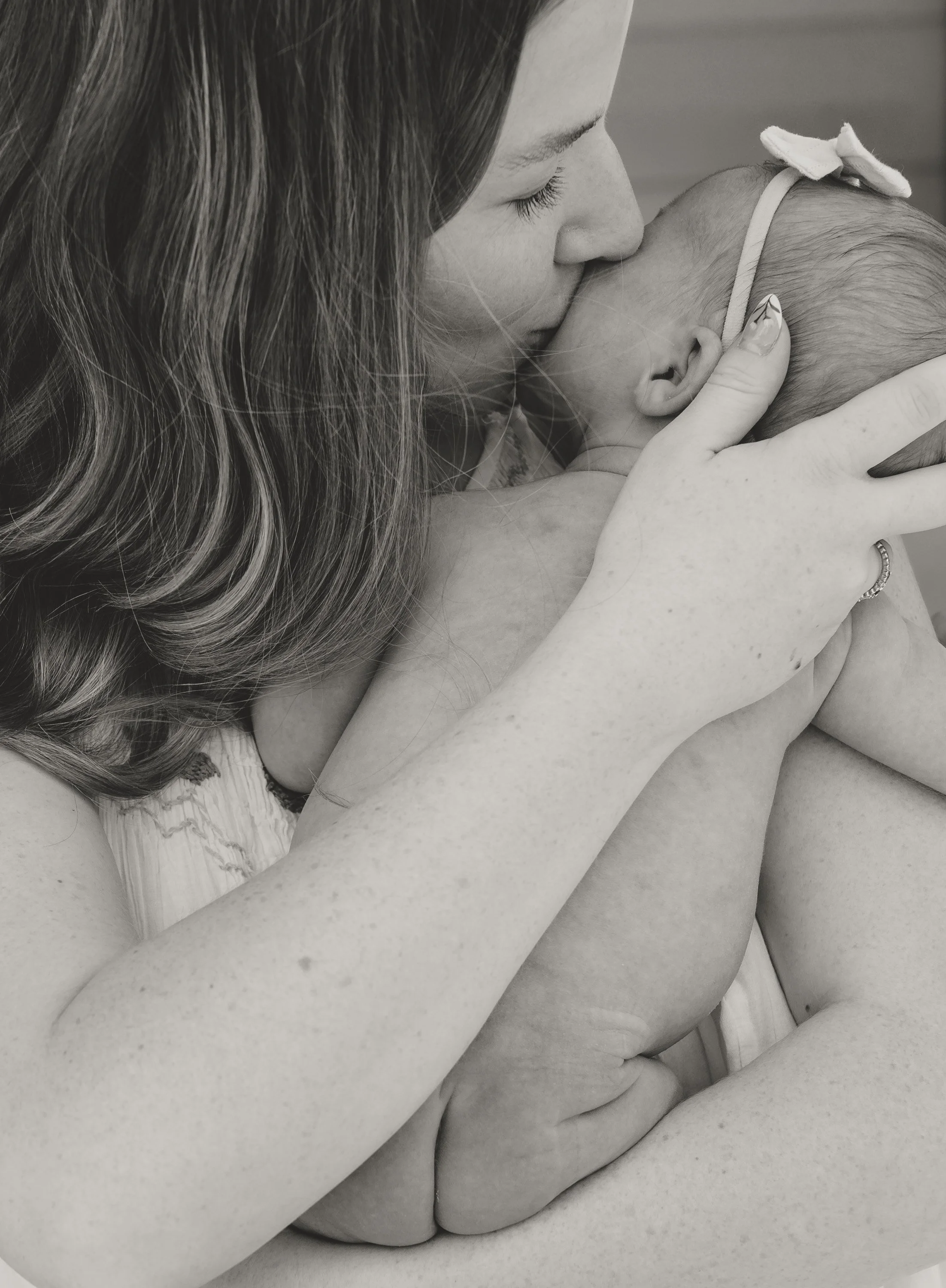 A woman kissing a baby on the forehead, both in a close embrace. lifestyle newborn photographer in Austin 