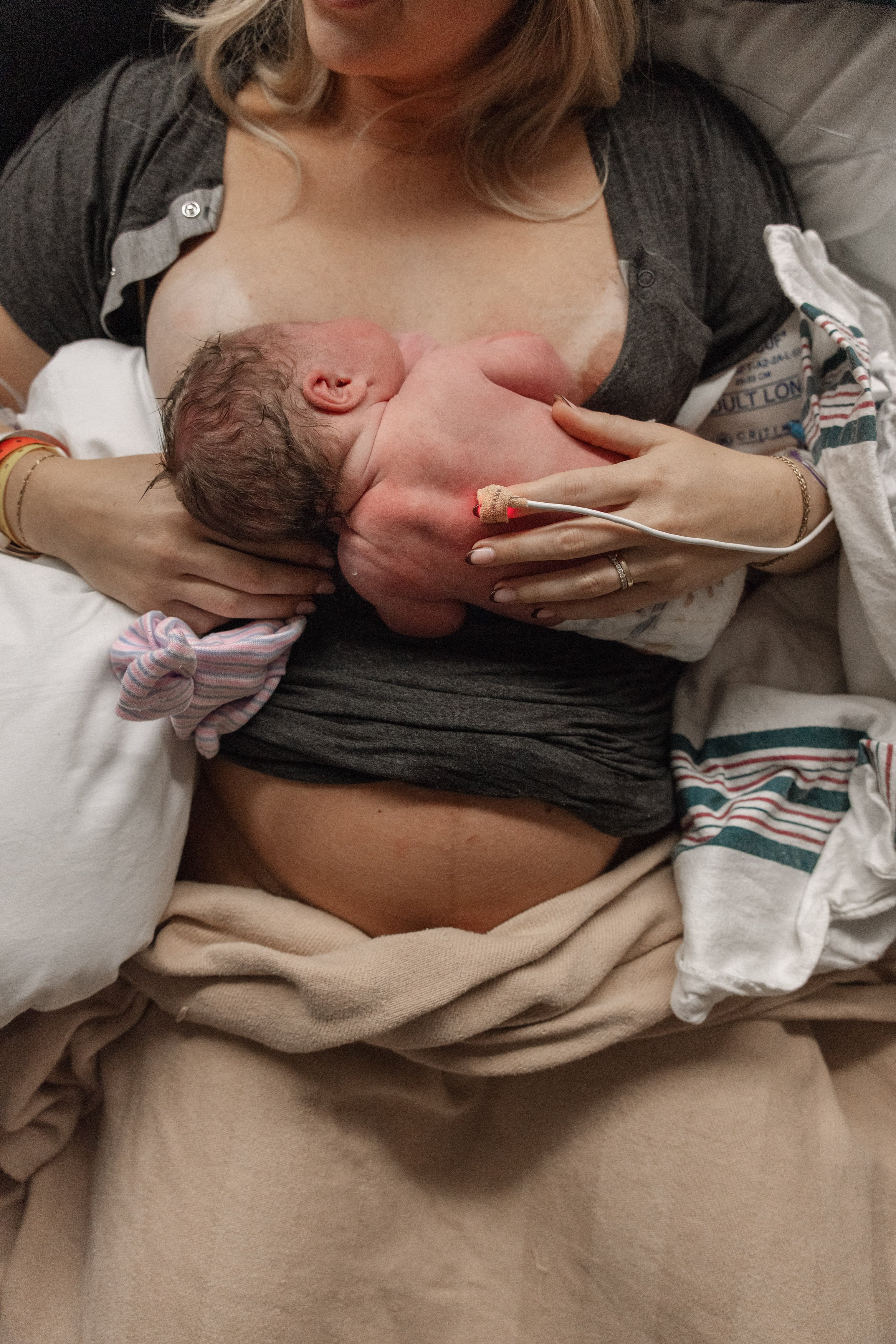 A woman in a hospital bed holding a newborn baby against her chest after childbirth. best birth photographer in Austin Texas