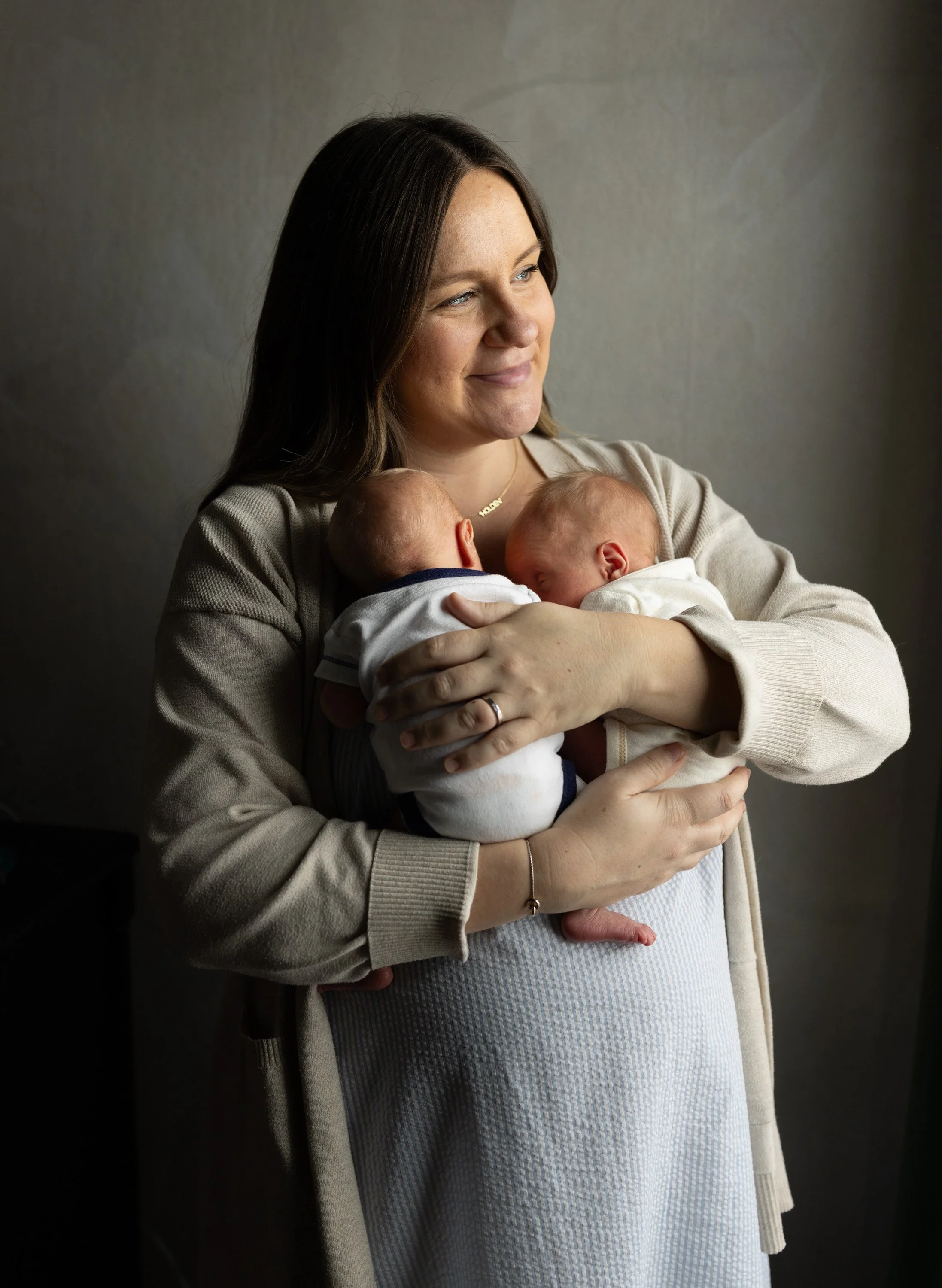 Woman holding two newborn babies, one sleeping on each arm, smiling gently. Austin Texas newborn photographer 