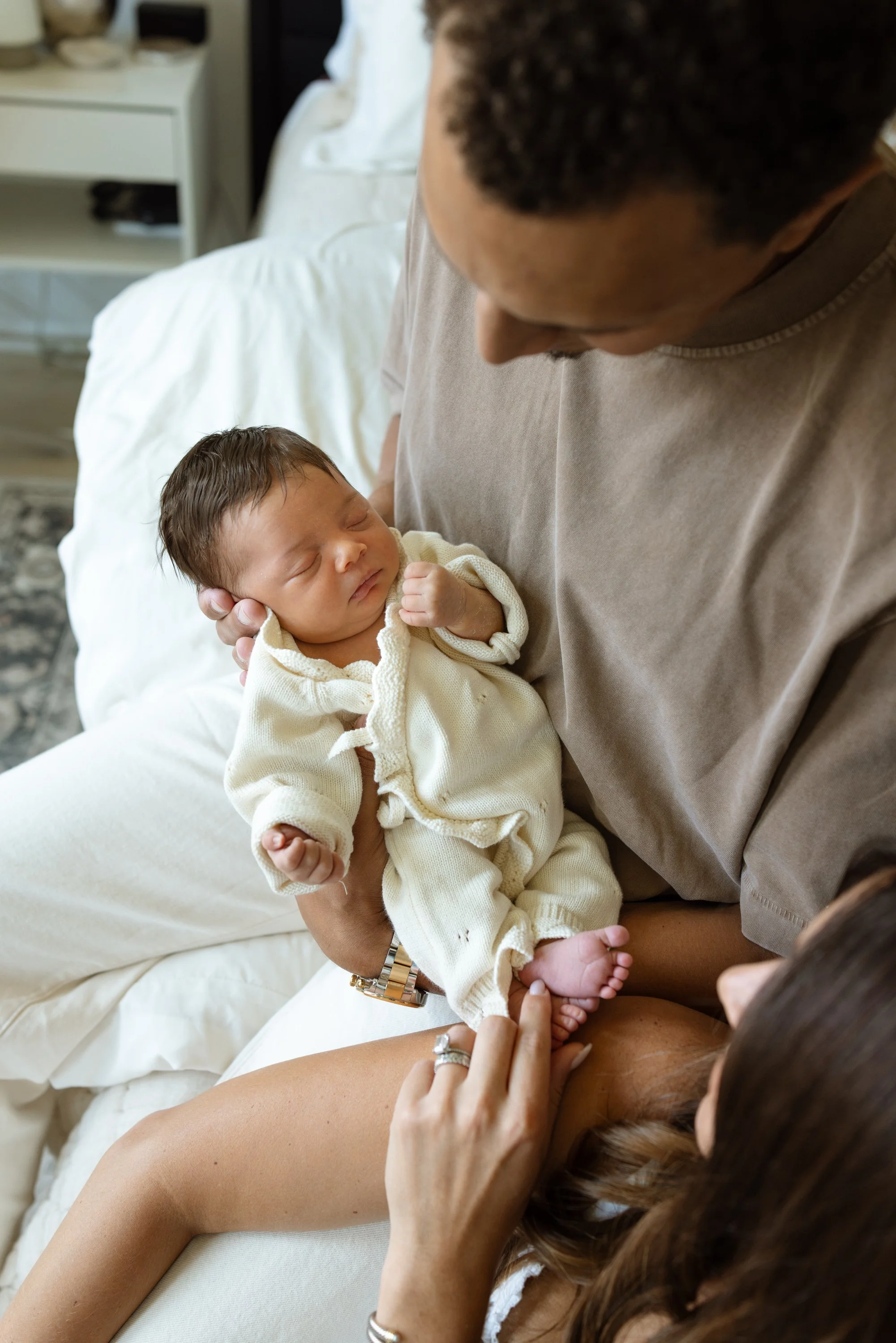 Austin newborn photographer captures mom and dad to a baby girl cuddling her on their bed. baby is wearing a knit outfit and is asleep
