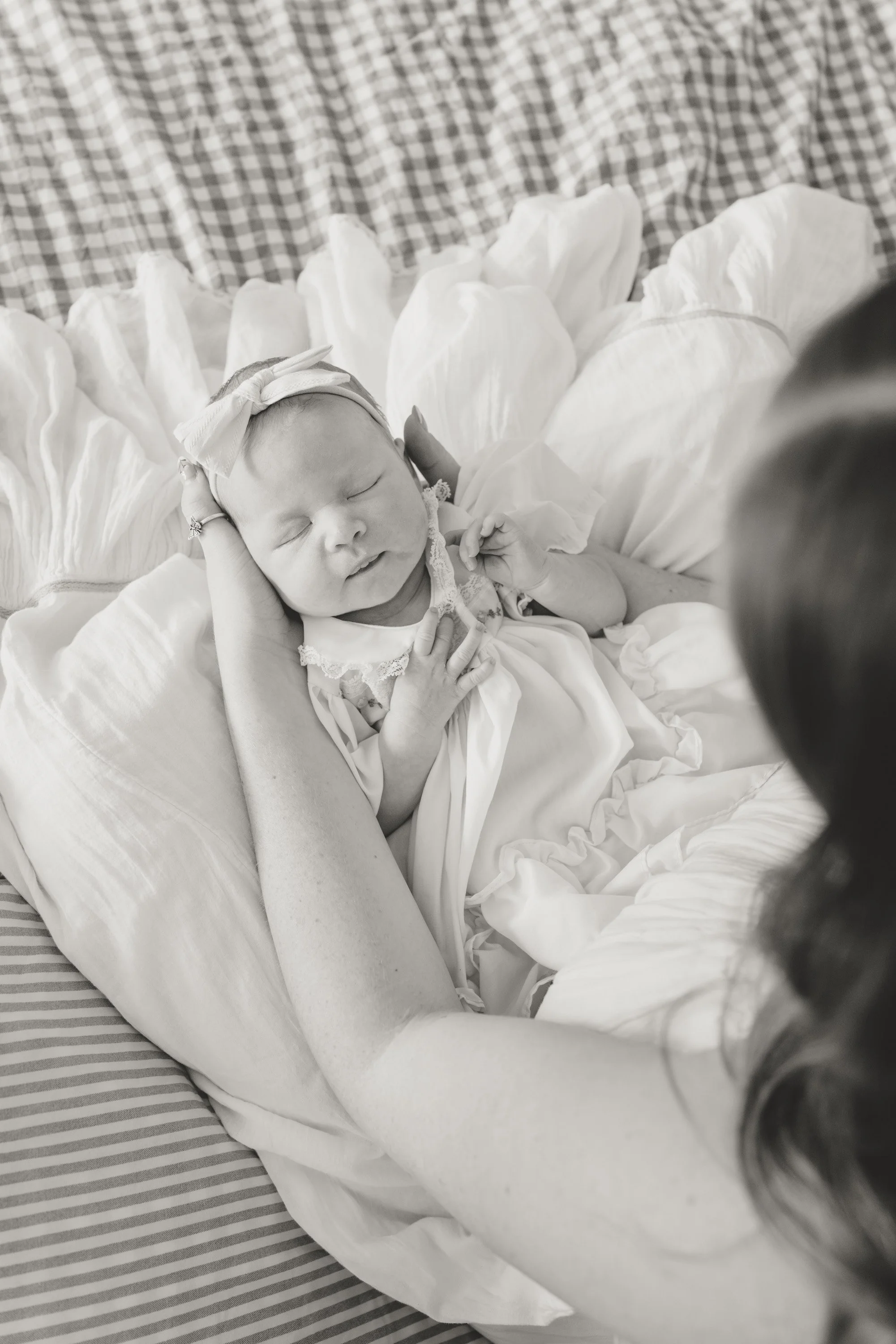 A newborn baby sleeping peacefully on a bed with a floral blanket and a striped sheet, wearing a headband with a large bow. newborn photography in dripping springs Texas
