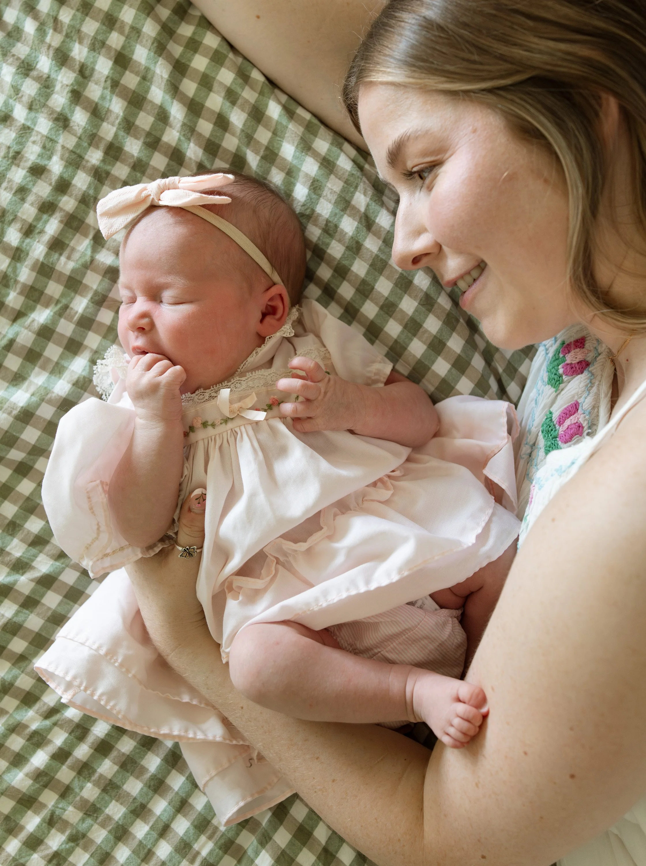 A woman and a baby lying on a green checkered blanket, smiling and looking at each other closely. documentary newborn photography Austin Texas 