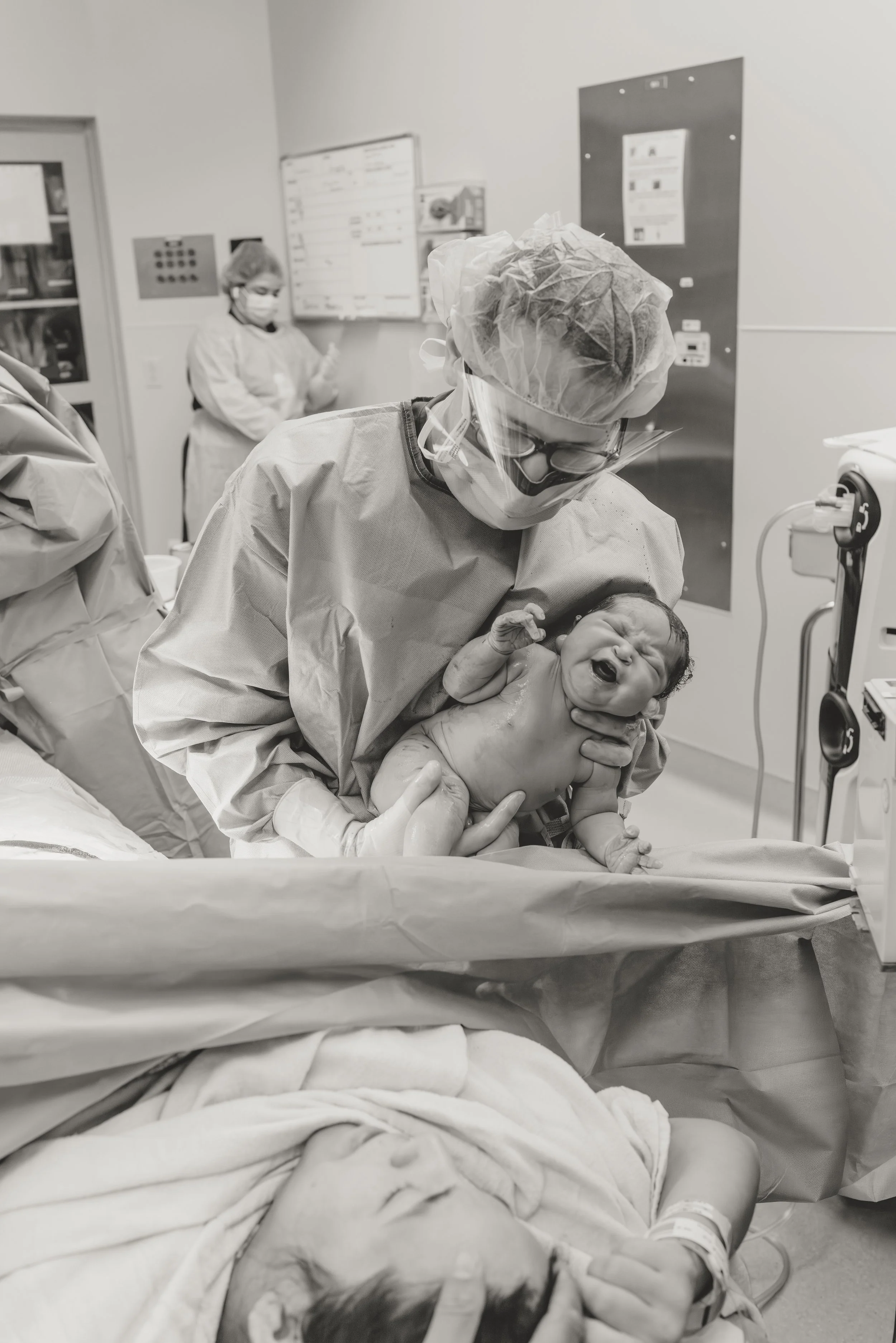 black and white photos shows a doctor holding a baby up to the drape right after being born via cesarean.
