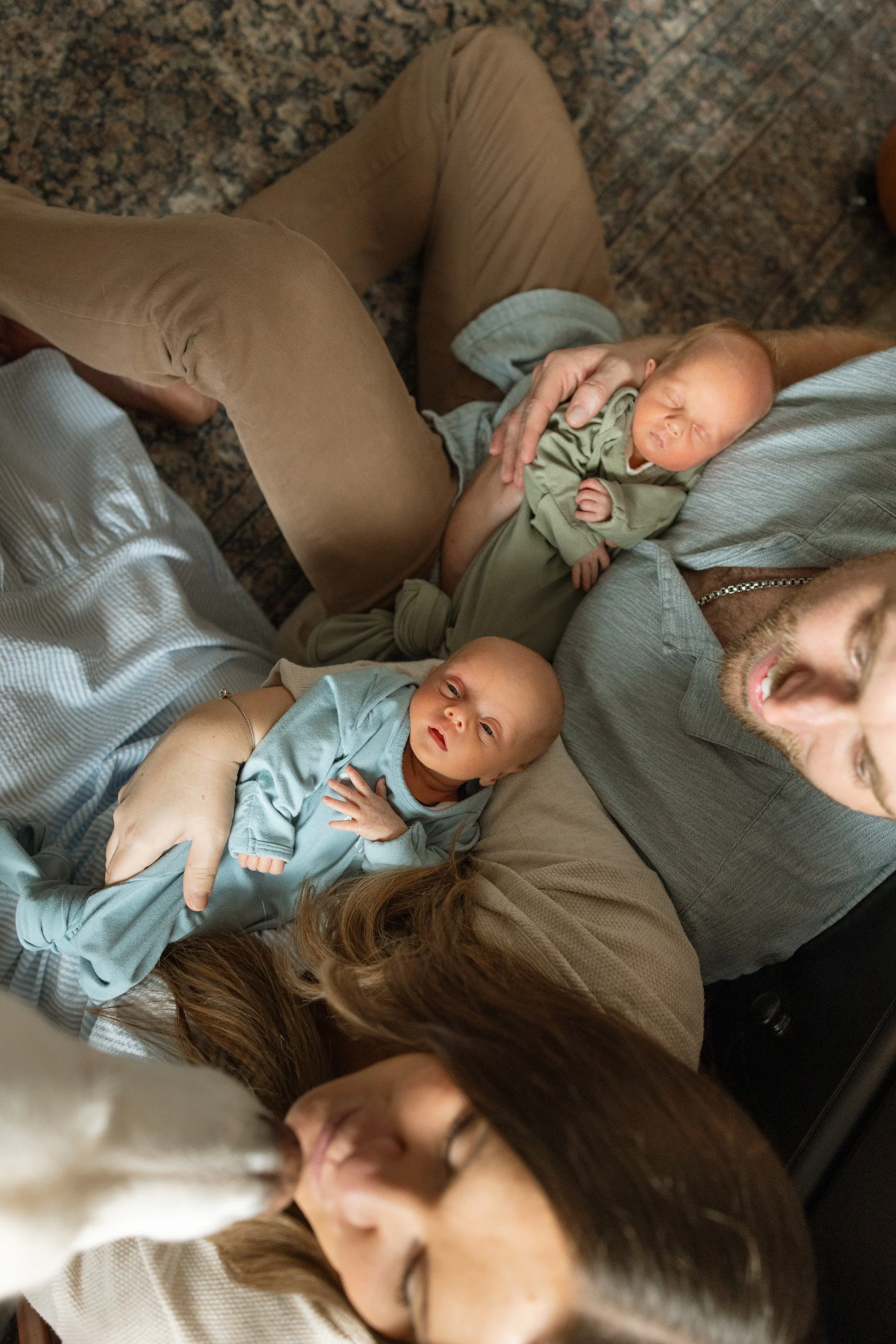 A group of people, including children and adults, lying on the floor with their heads close together, some with eyes closed, in a relaxed, affectionate pose. newborn photography in Austin Texas